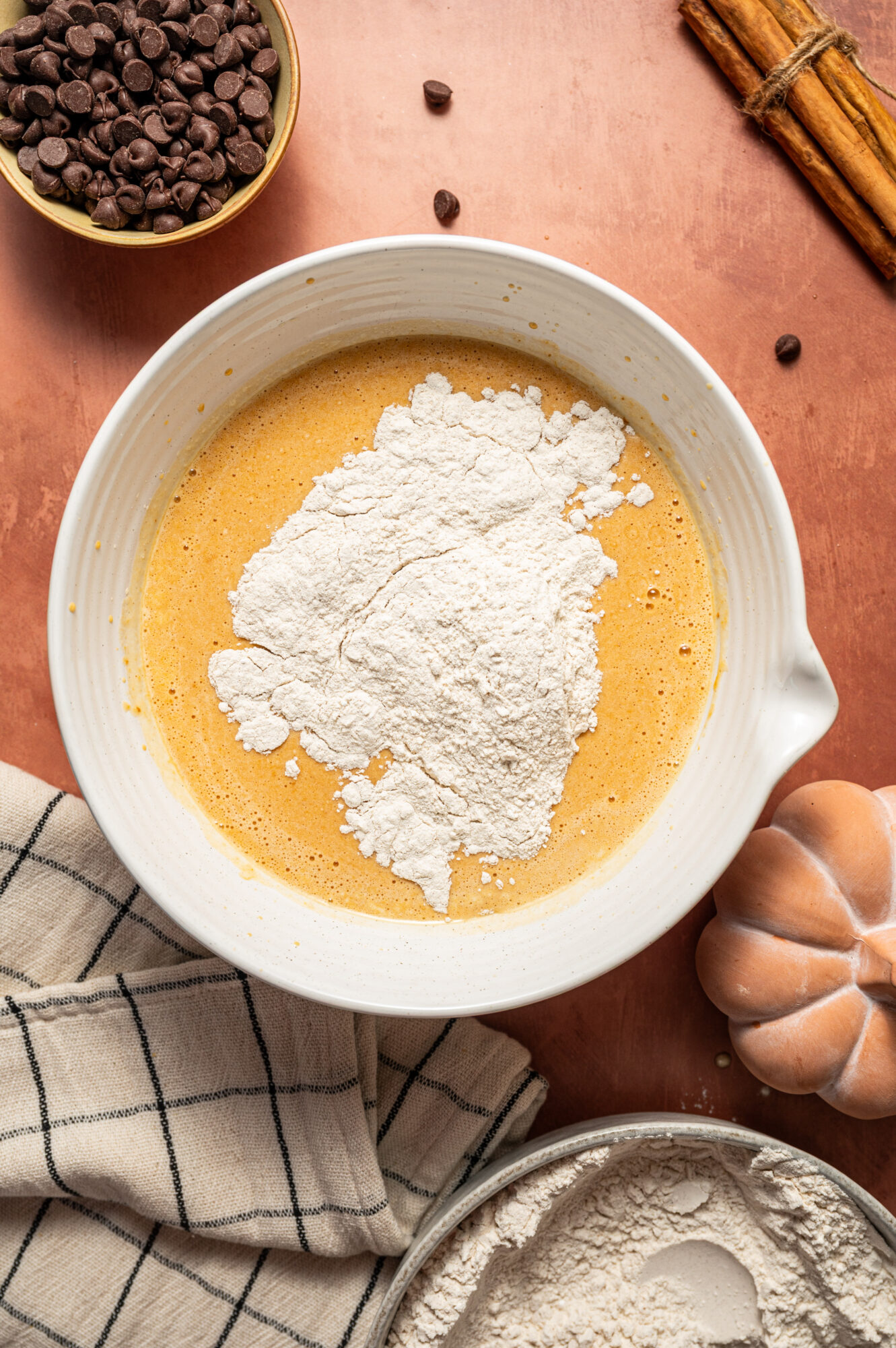 Adding the dry ingredients to the wet ingredients in a large white mixing bowl.