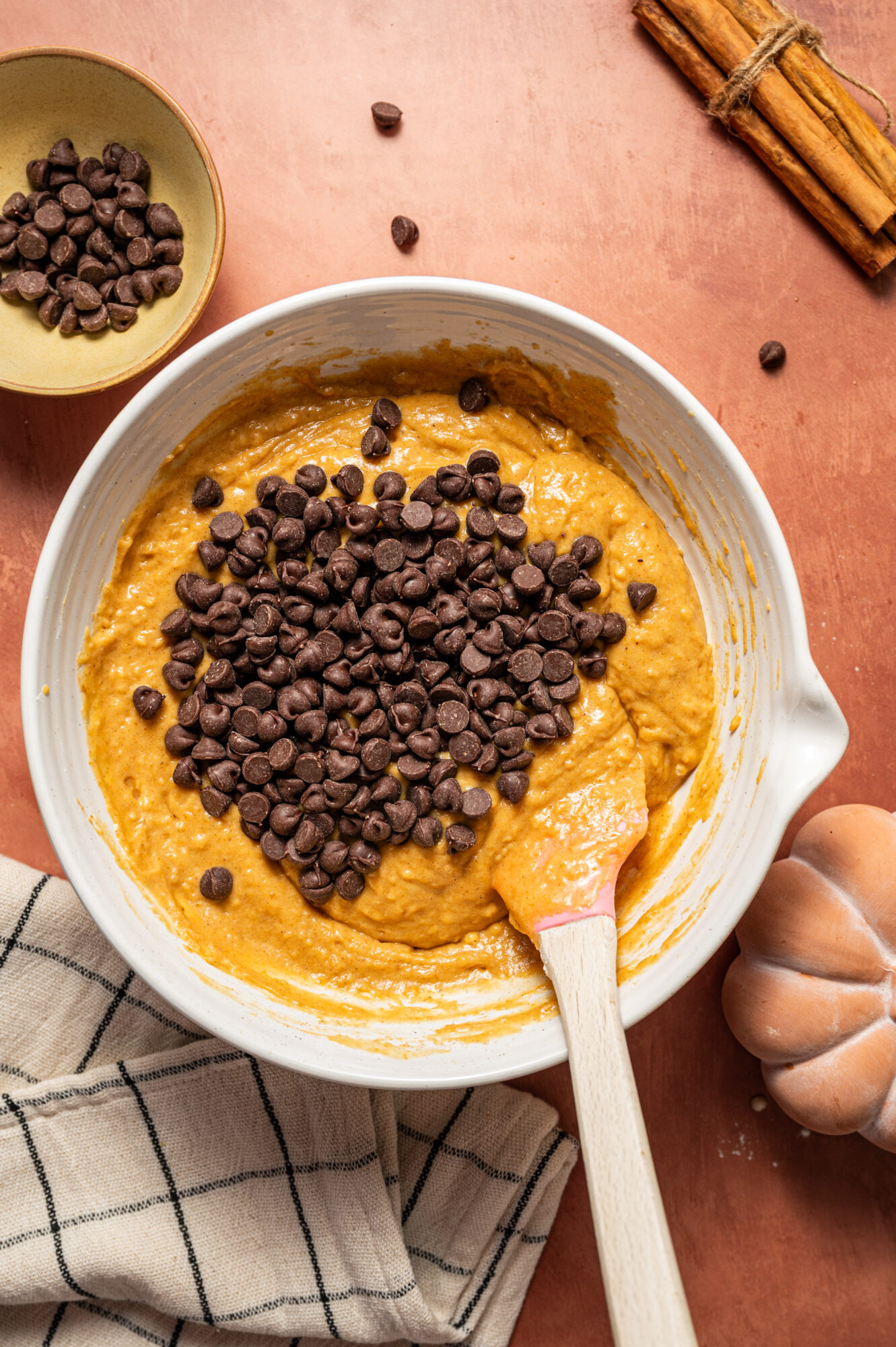 Mixing chocolate chips into a mixing bowl of pumpkin muffin batter.