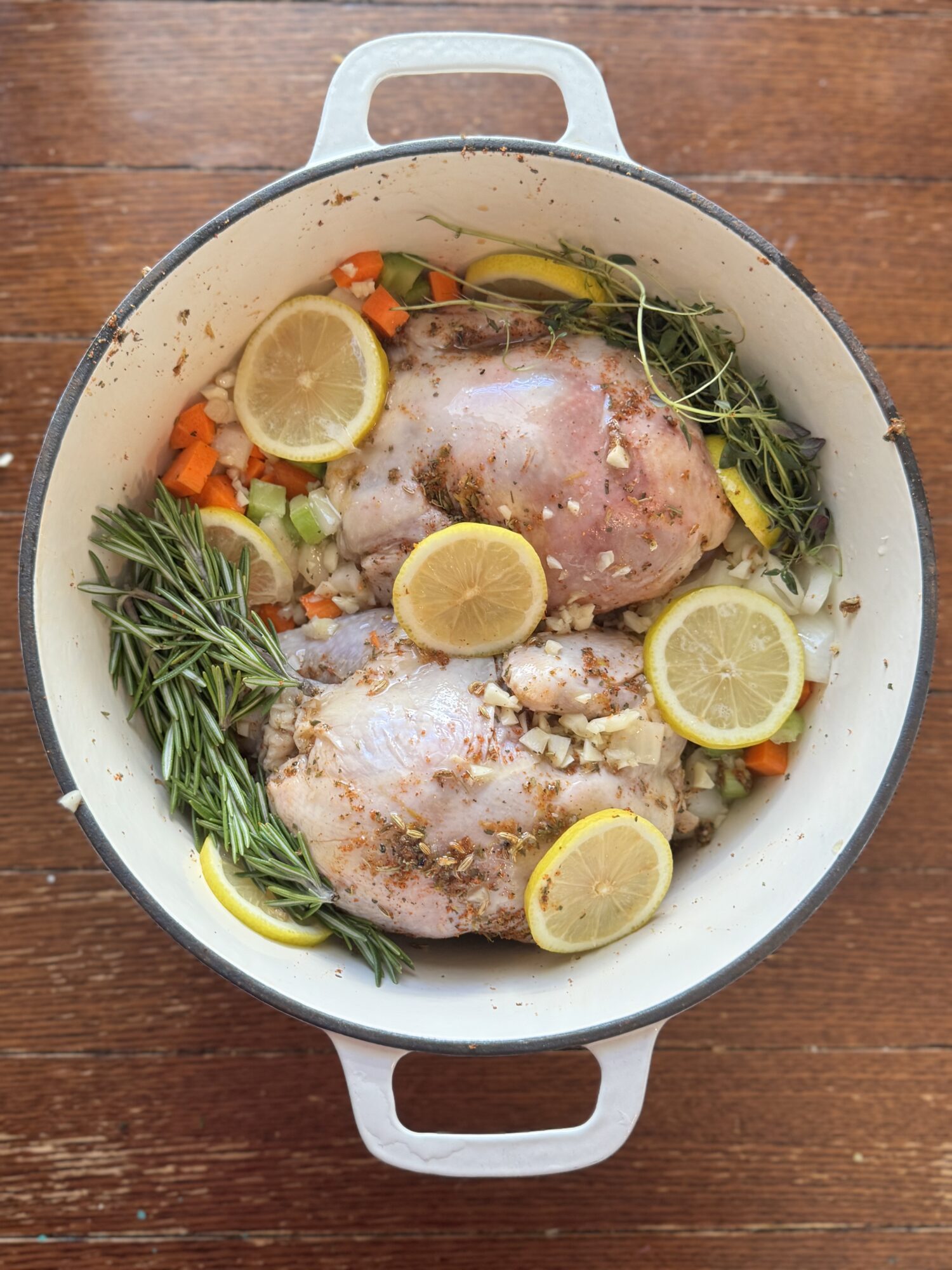 Cornish hens in a Dutch oven with lemon slices and rosemary ready to roast.