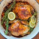 Cornish hens in a Dutch oven garnished with lemon slices and rosemary.