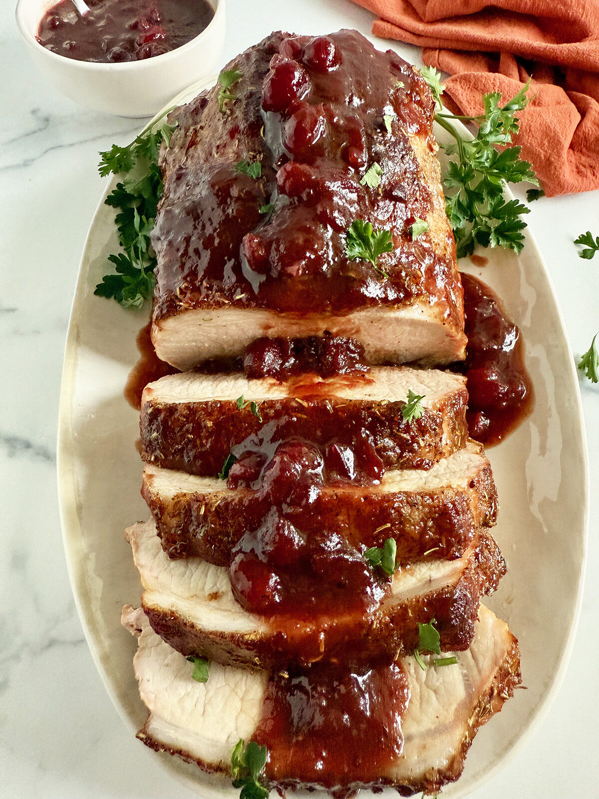 Pork loin roast sliced and served on a platter with cranberry/balsamic sauce.
