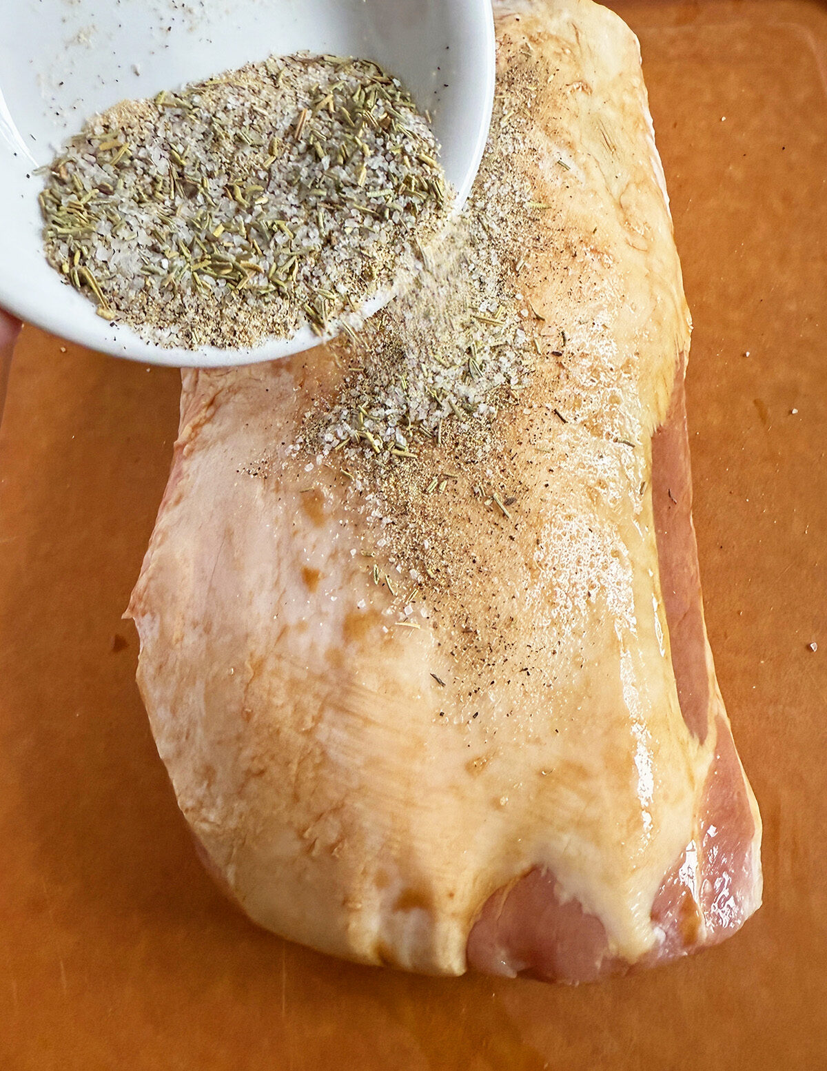 Adding seasonings to a pork loin roast.