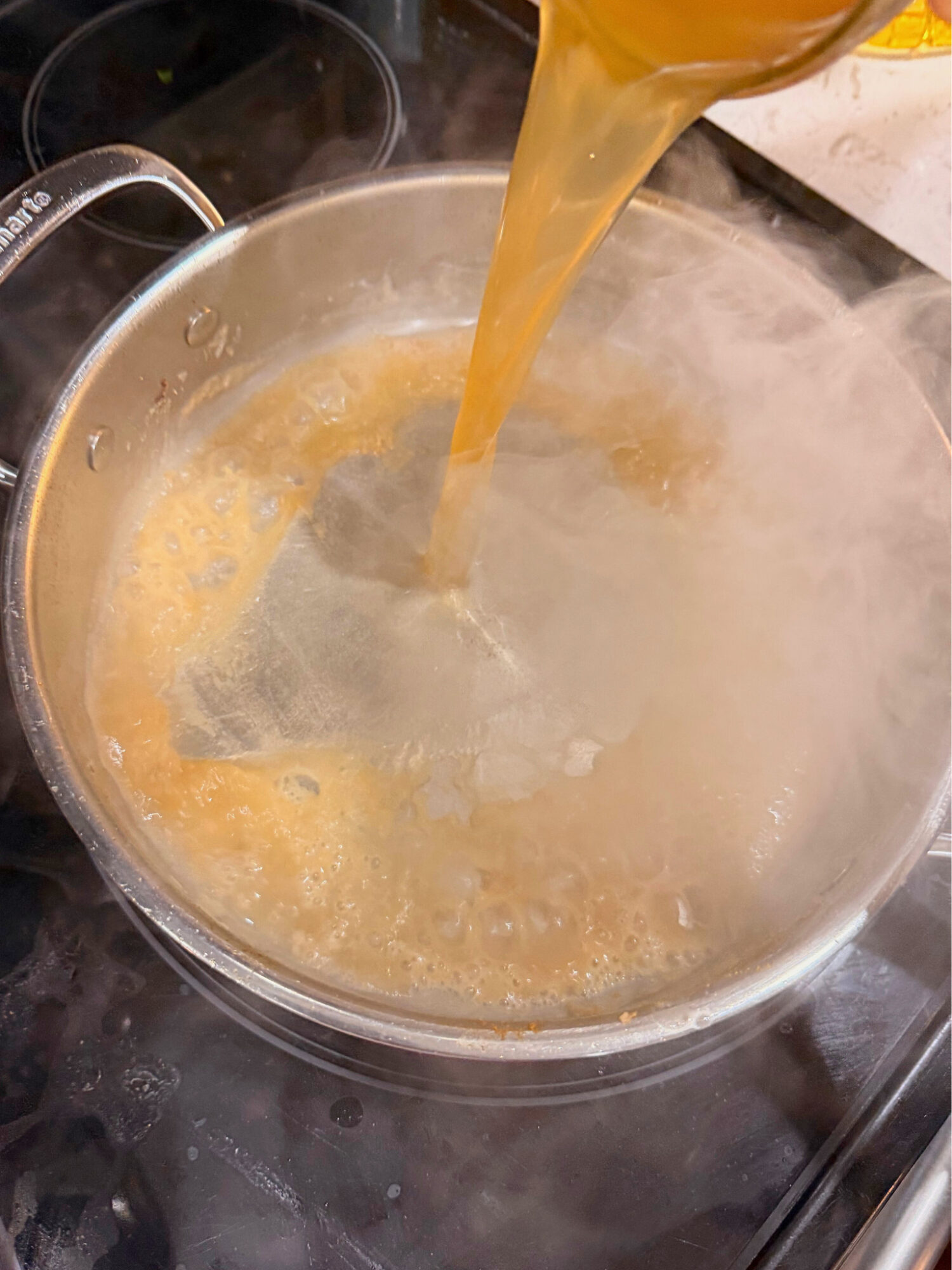 Pouring broth into a pot over the stove.