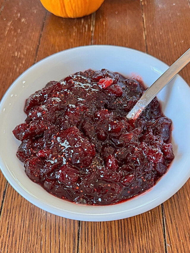 Homemade cranberry sauce in a white bowl with a spoon.