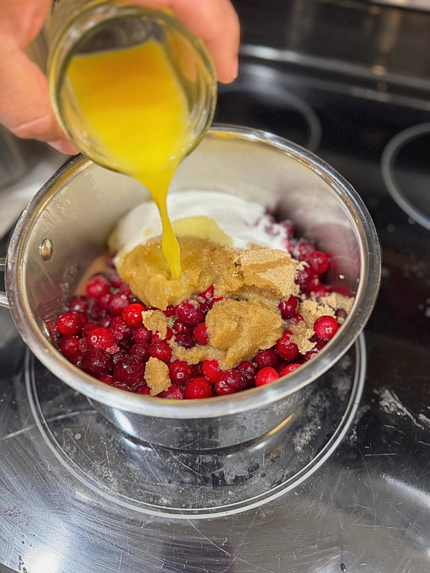 Adding orange juice to a pot of ingredients for homemade cranberry sauce.