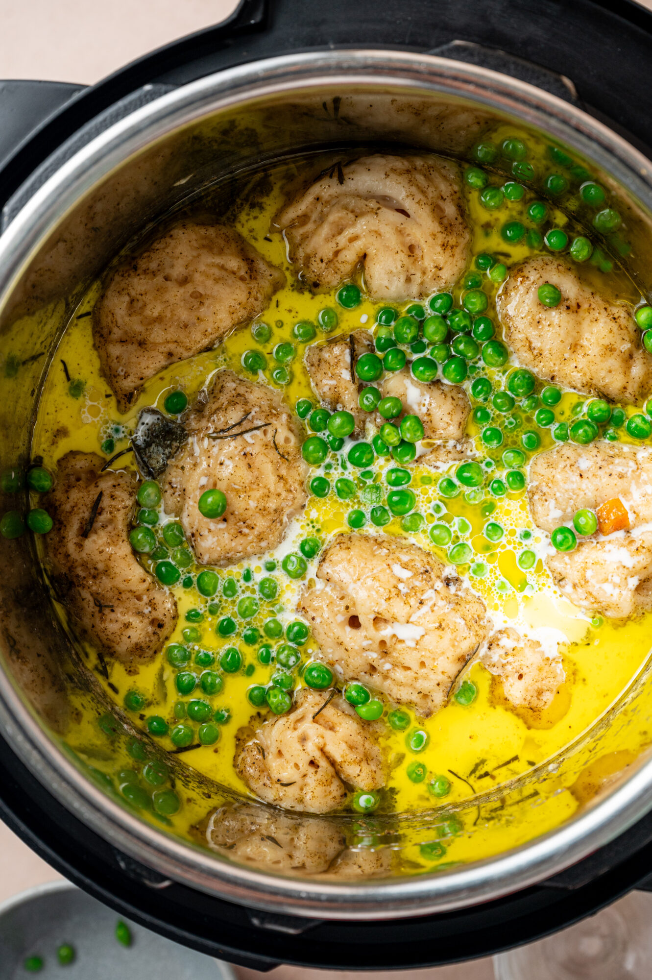 Cooked chicken simmering in a broth with peas.