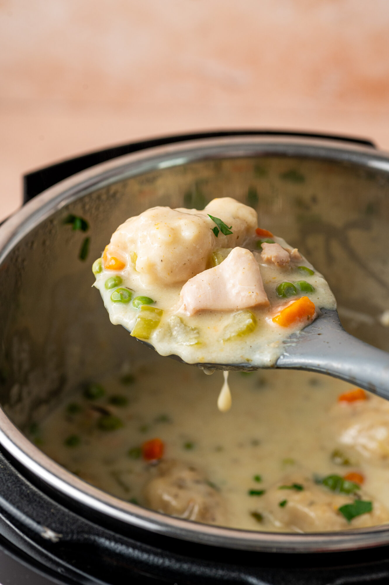 A spoonful of Instant Pot chicken and dumplings hovering over a pot.