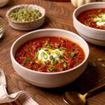 Pumpkin chili in a white bowl with sour cream and green onions.