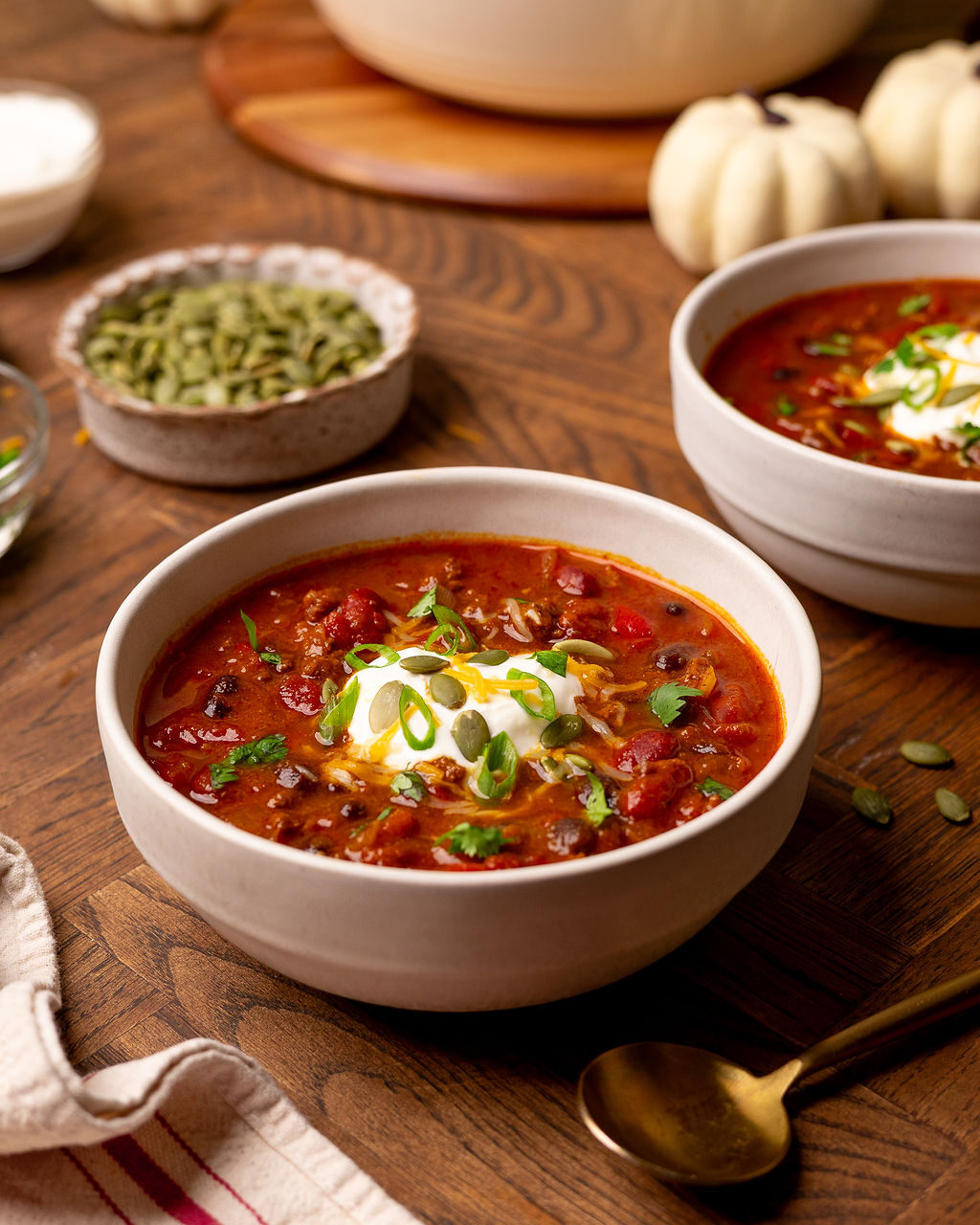 Pumpkin chili in a white bowl with sour cream and green onions.
