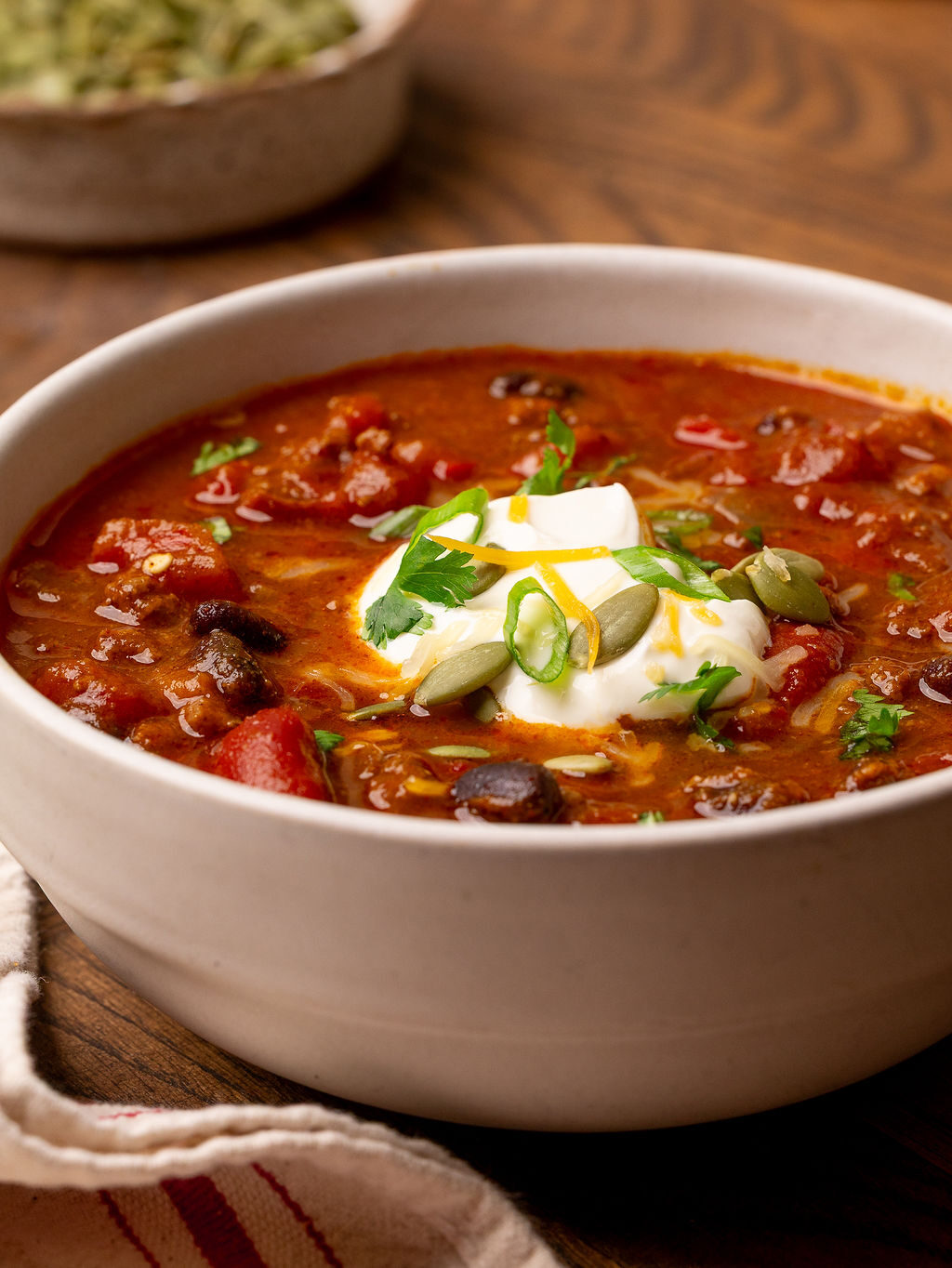 Close-up of a bowl of pumpkin chili with sour cream and green onions.