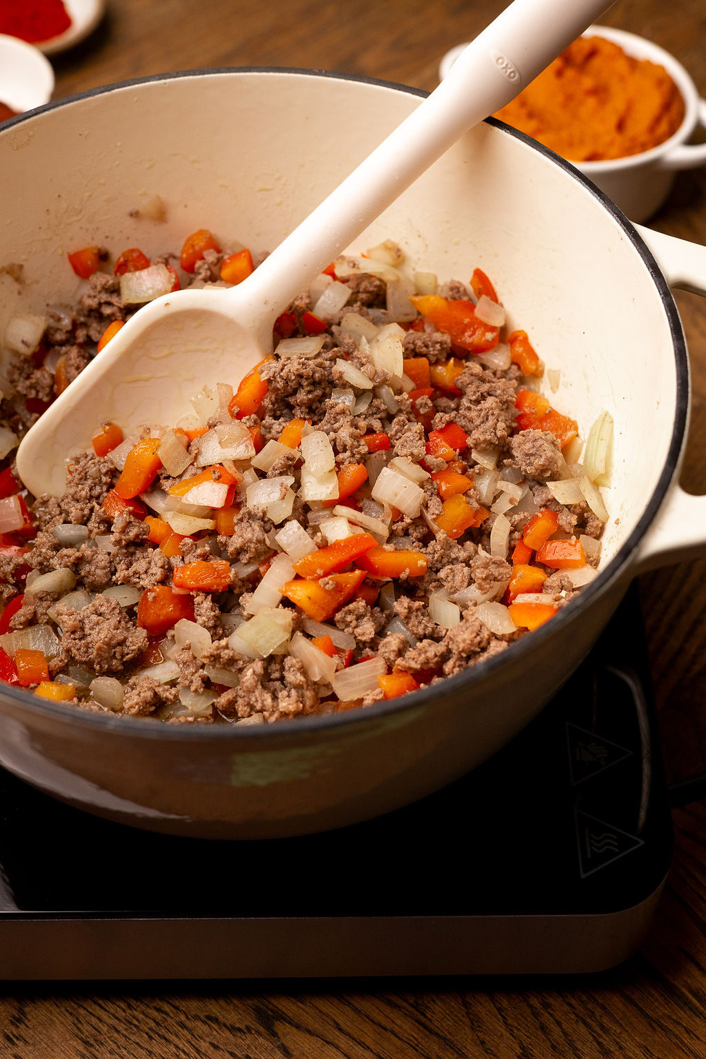 Mixing chopped veggies with browned beef in a Dutch oven.