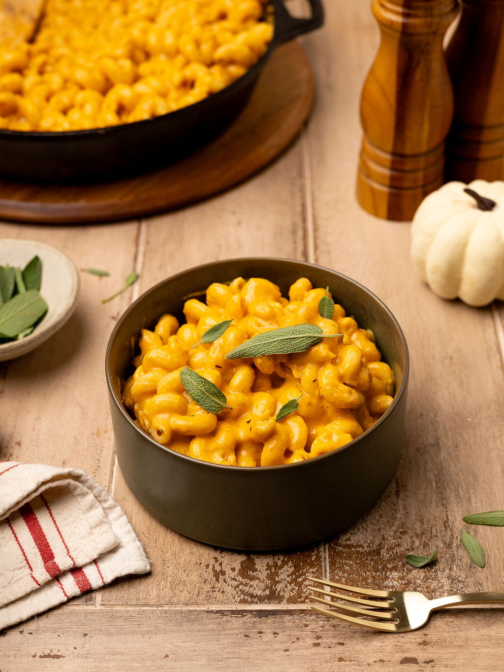 Pumpkin mac and cheese in a black bowl garnished with sage leaves.