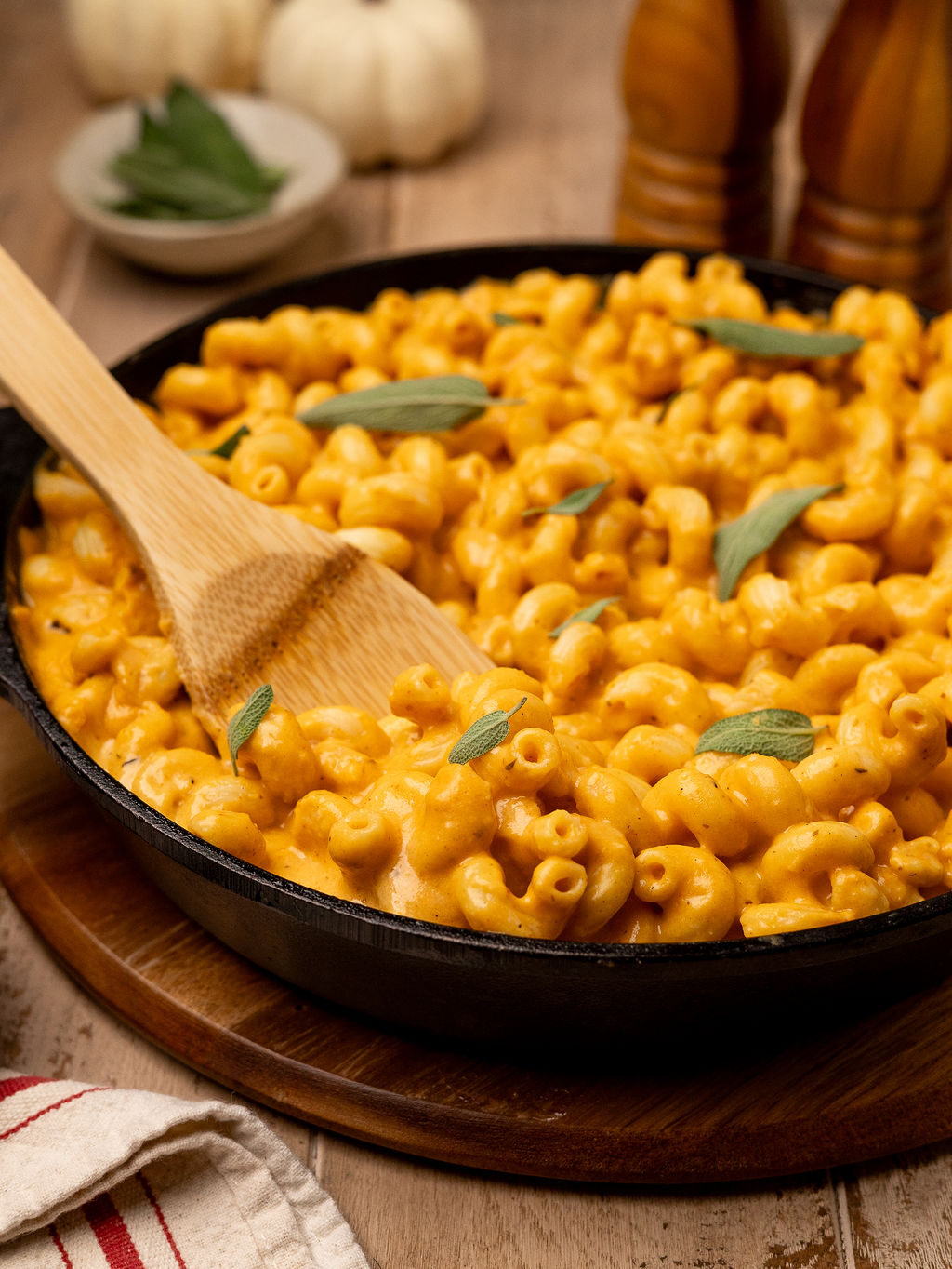Dipping a wooden spoon in a cast iron pan of pumpkin mac and cheese.