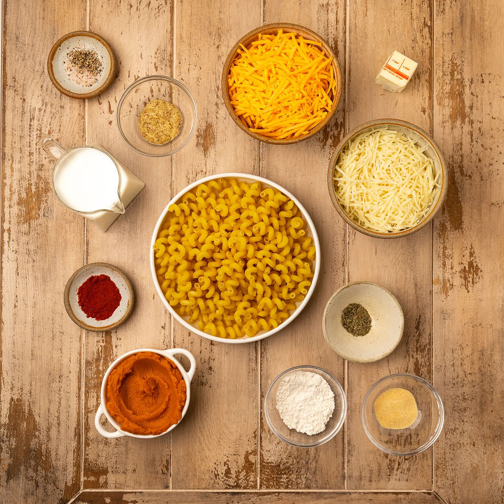 Ingredients for pumpkin mac and cheese over a light wooden surface.