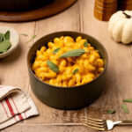 Pumpkin mac and cheese in a black bowl garnished with sage leaves.