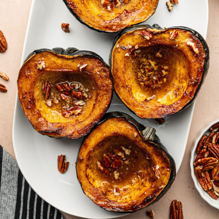 Roasted acorn squash on a white serving tray topped with pecans.