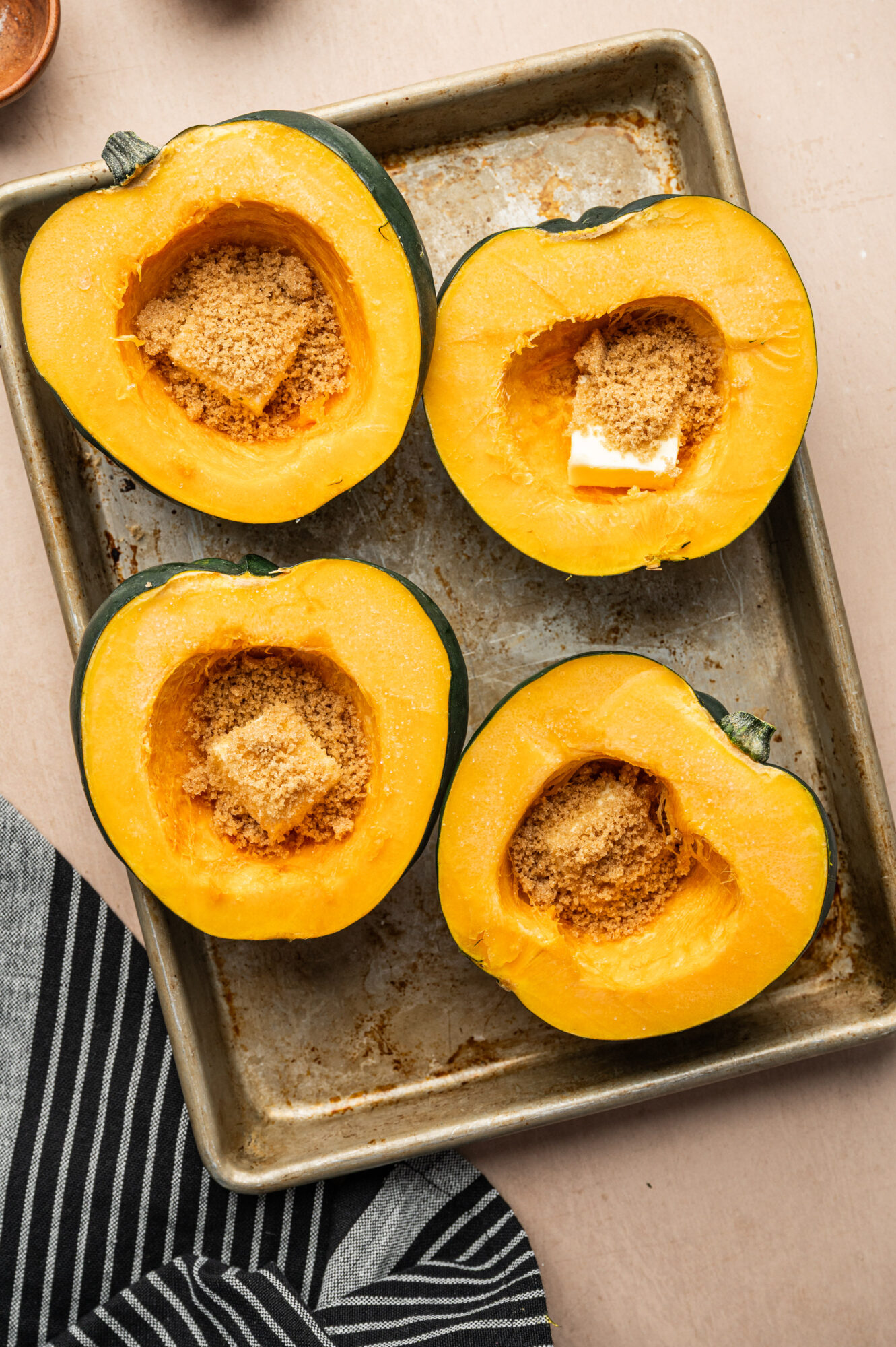 Acorn squash on a baking sheet with brown sugar and butter ready to bake.