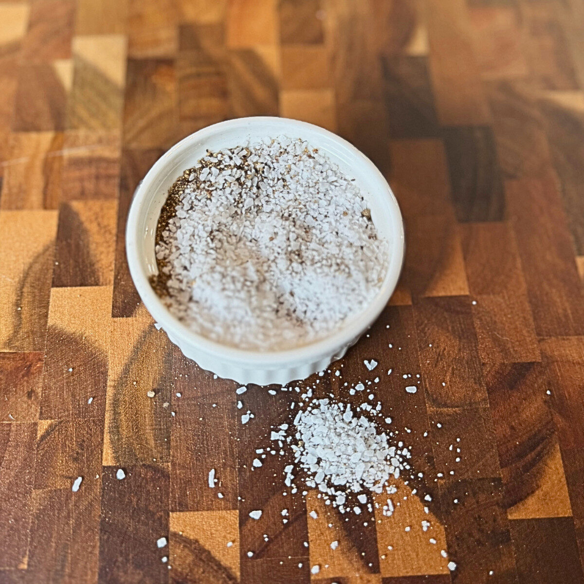 Salt and pepper mix in a shallow dish over a wooden surface.