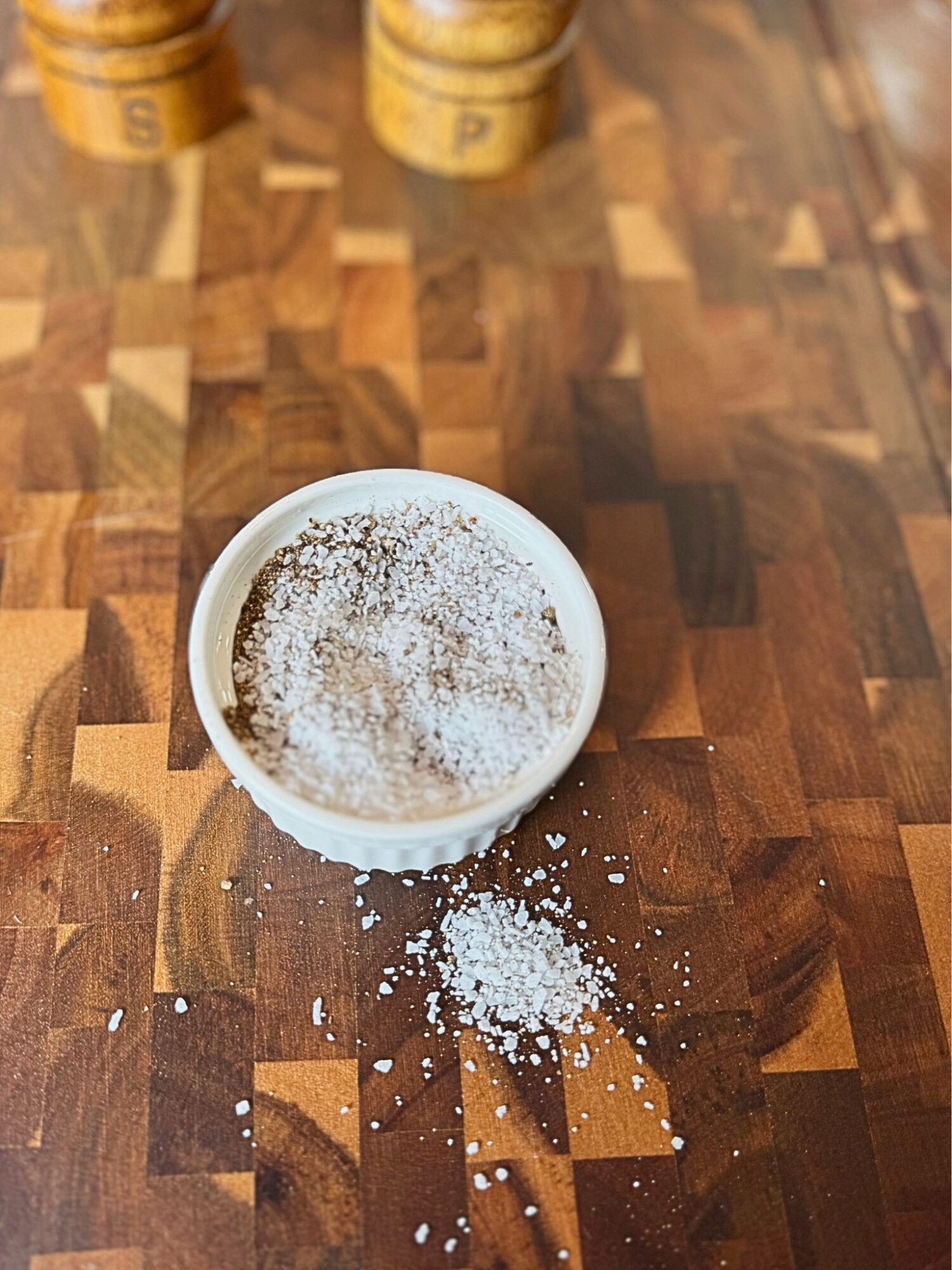 Salt and pepper mix in a shallow dish over a wooden surface.