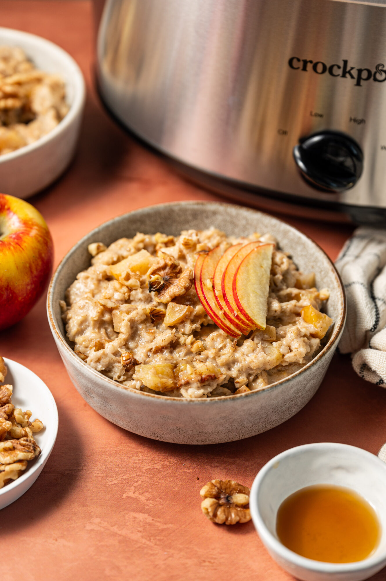 A bowl of apple cinnamon oatmeal in front of a slow cooker topped with apple slices.