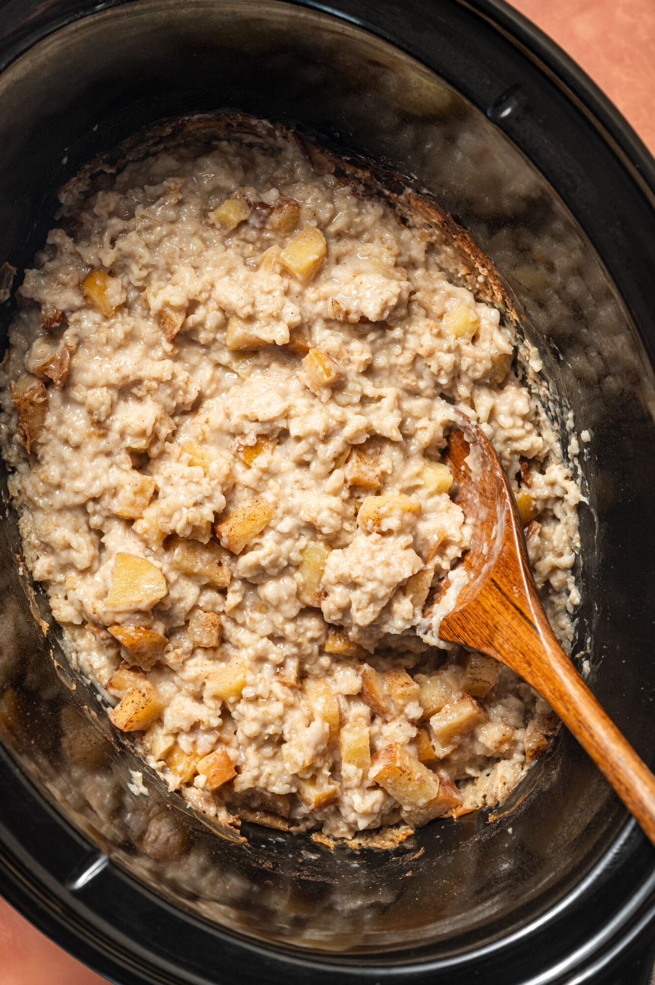 Apple cinnamon oatmeal in a slow cooker with a wooden spoon.