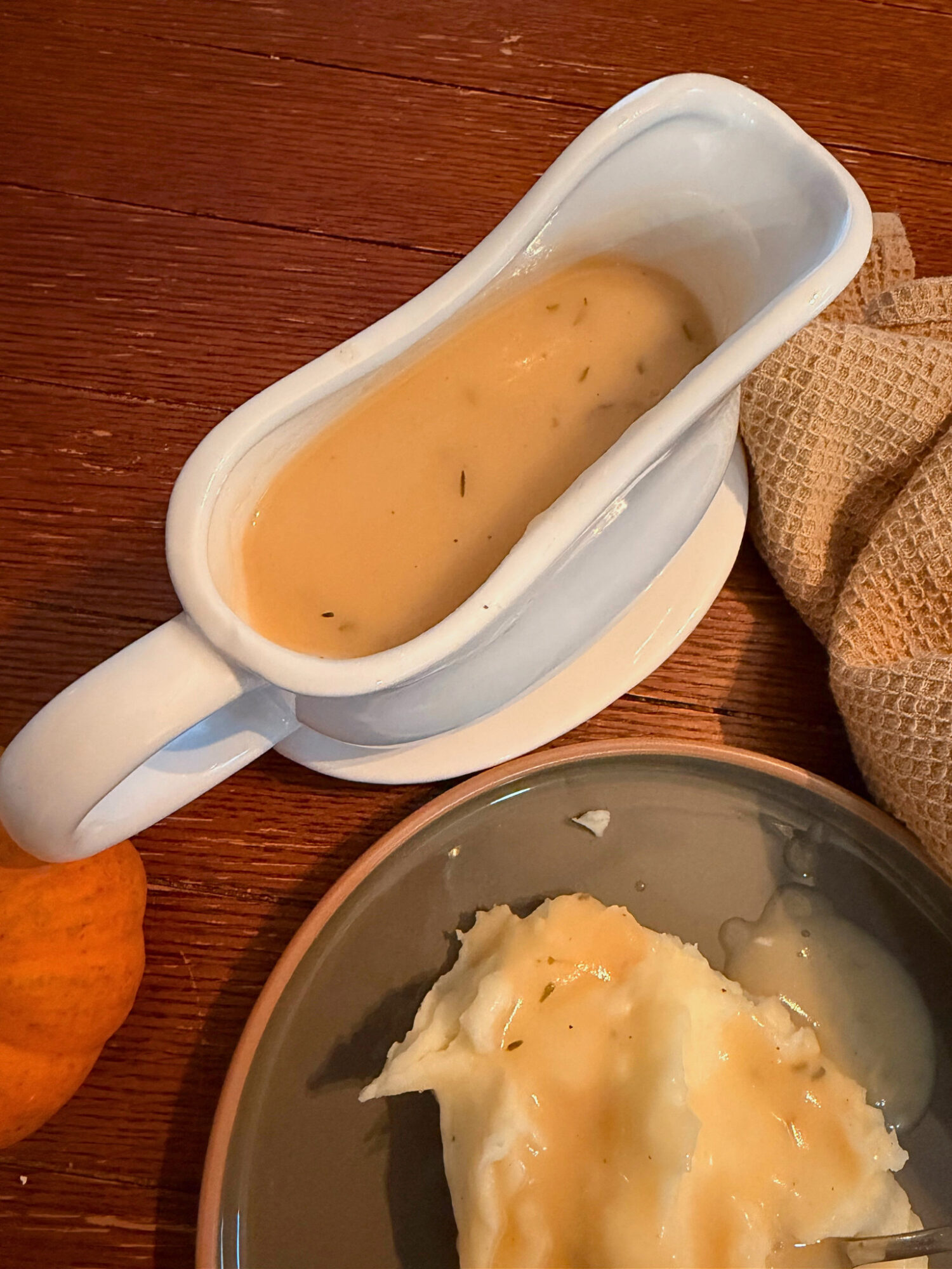 A turkey boat filled with turkey gravy with a plate of mashed potatoes.