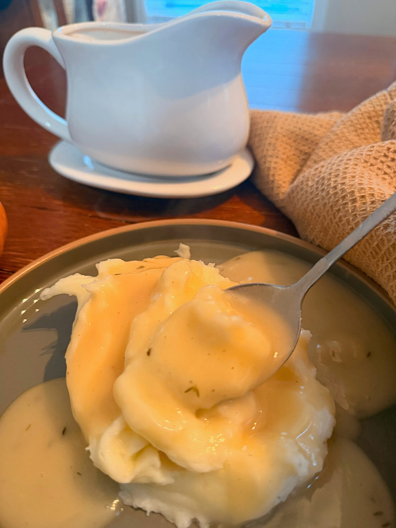 A spoon dipping into a plate of mashed potatoes with gravy.