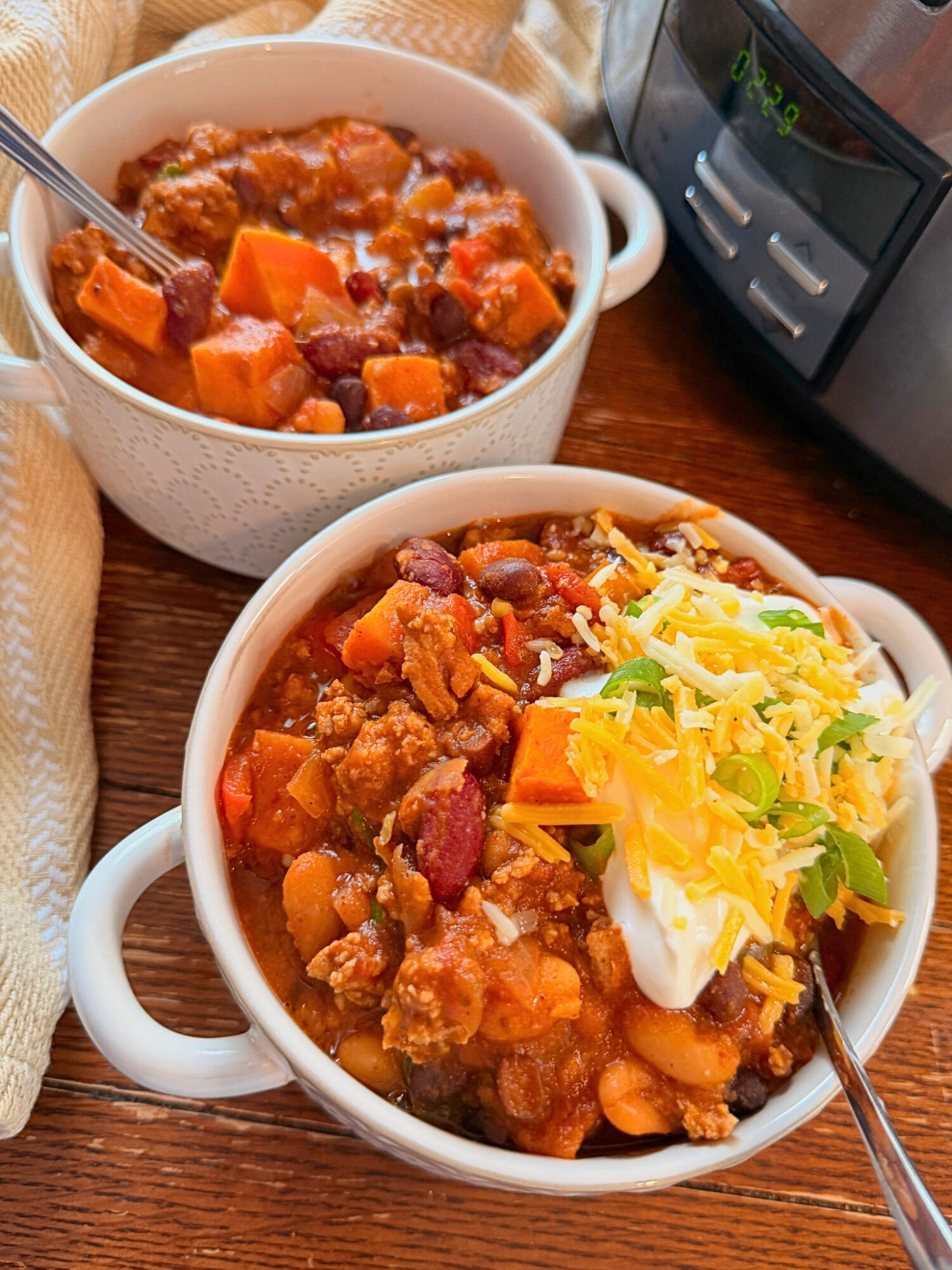 Two bowls of turkey and sweet potato chili with sour cream, cheese, and chives.