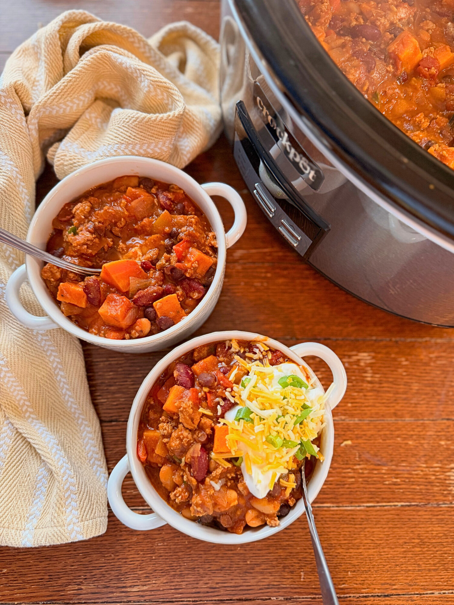 Two bowls of turkey and sweet potato chili next to the slow cooker on a wooden table.