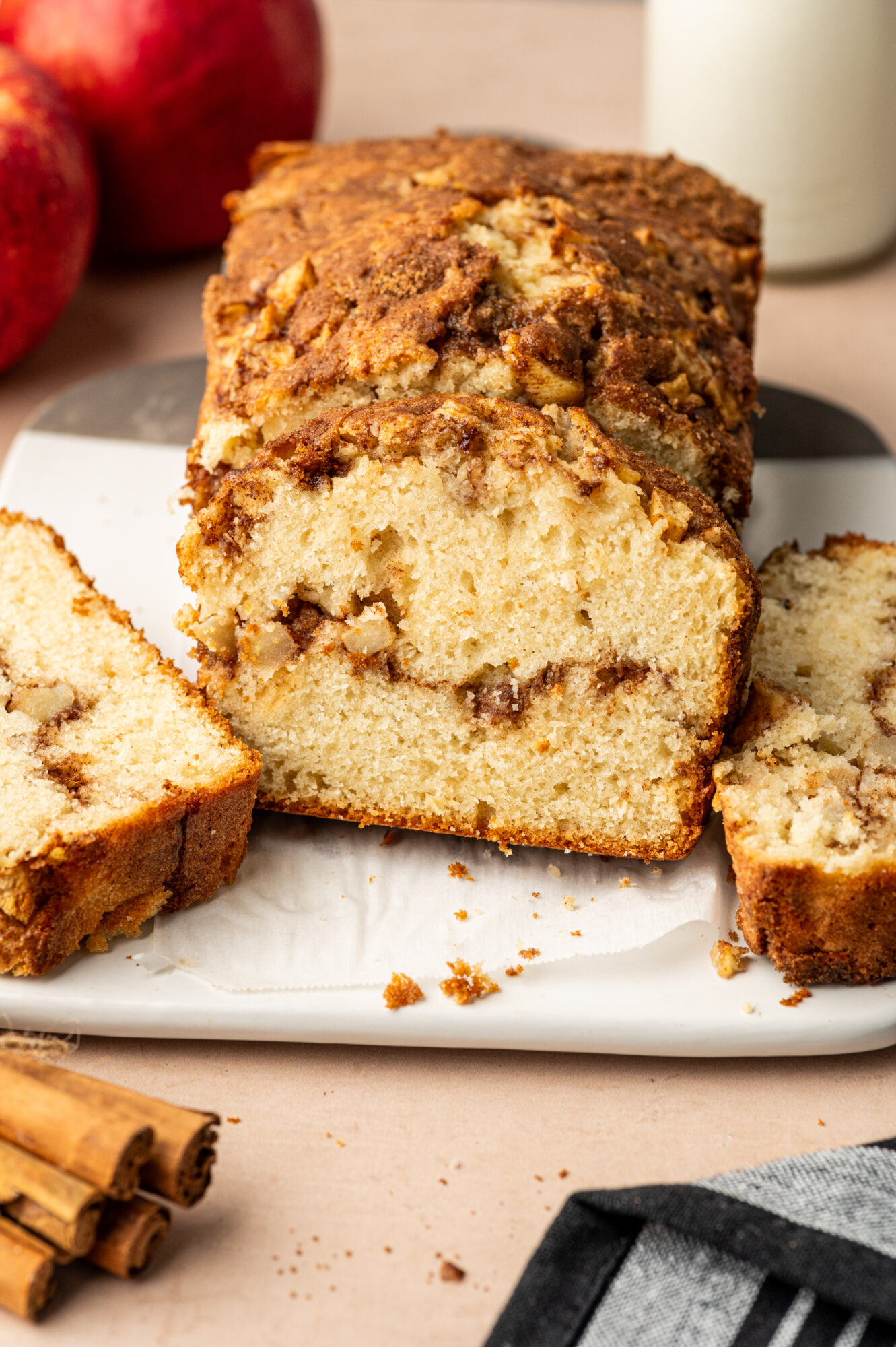 Apple cinnamon bread loaf sliced on a white plate showing a cinnamon swirl.