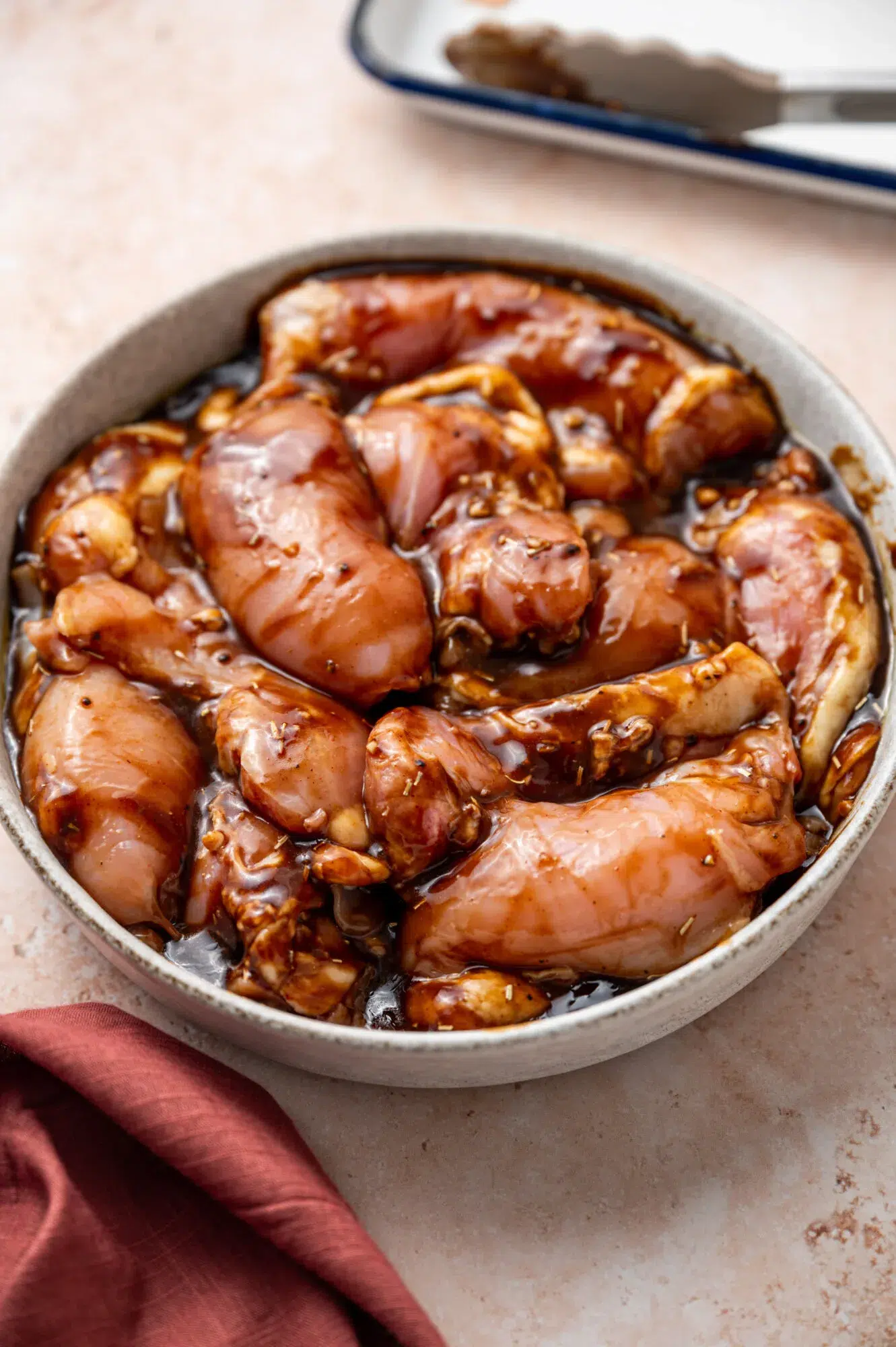 A white bowl of raw chicken thighs coated in a balsamic Dijon mustard glaze.