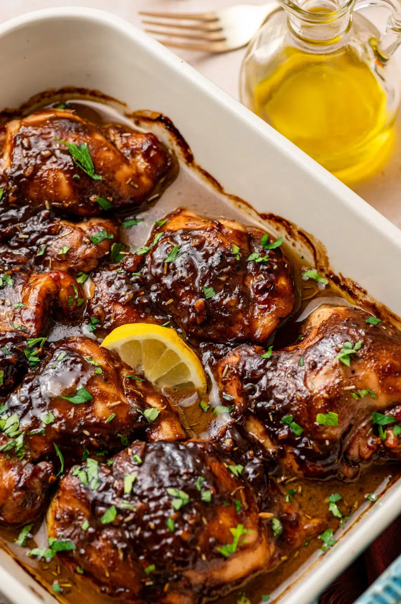 Close-up of balsamic Dijon mustard chicken thighs in a baking dish with a lemon wedge.
