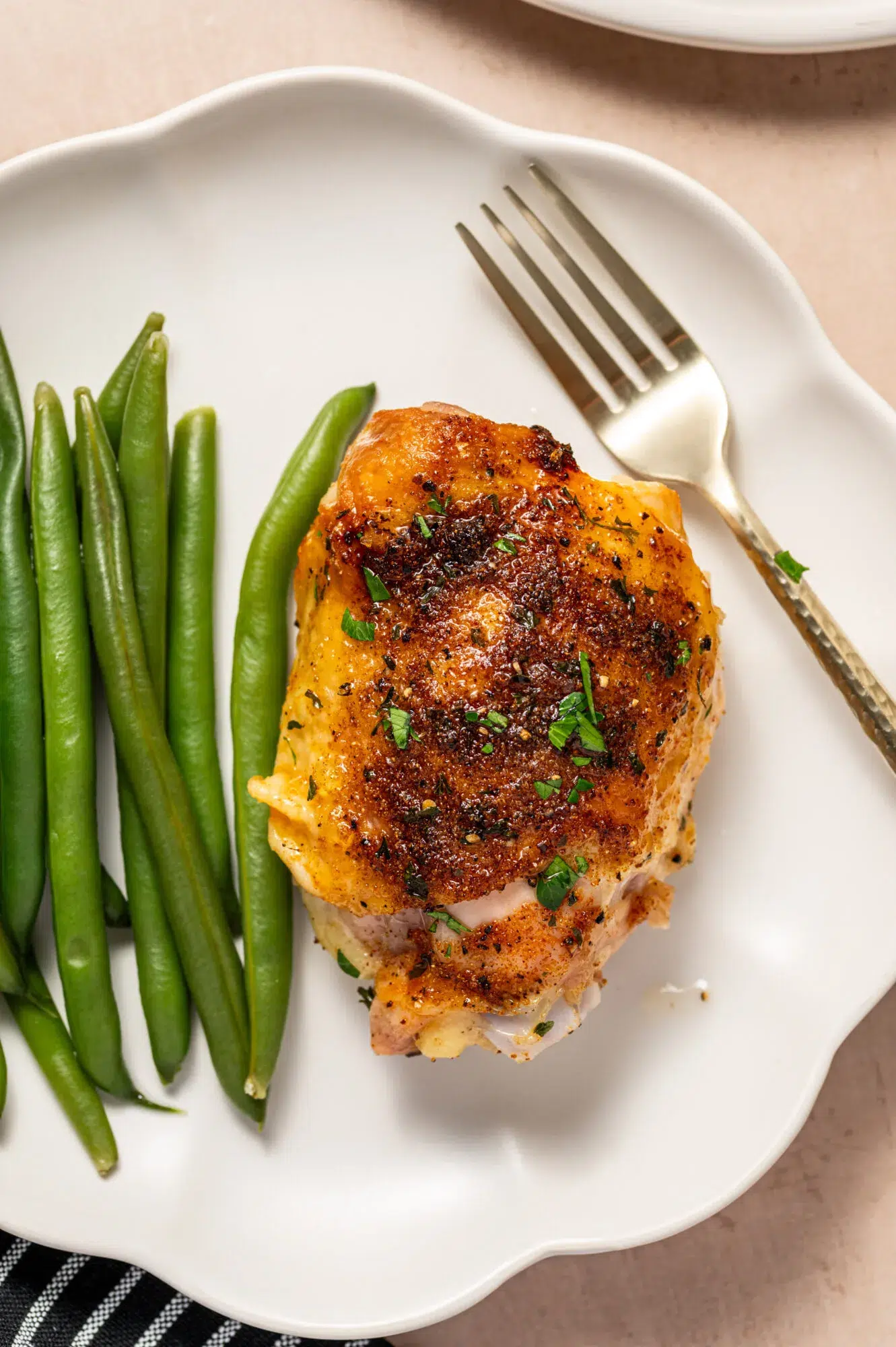 Aerial view of an oven roasted chicken thigh on a white plate with a side of green beans.