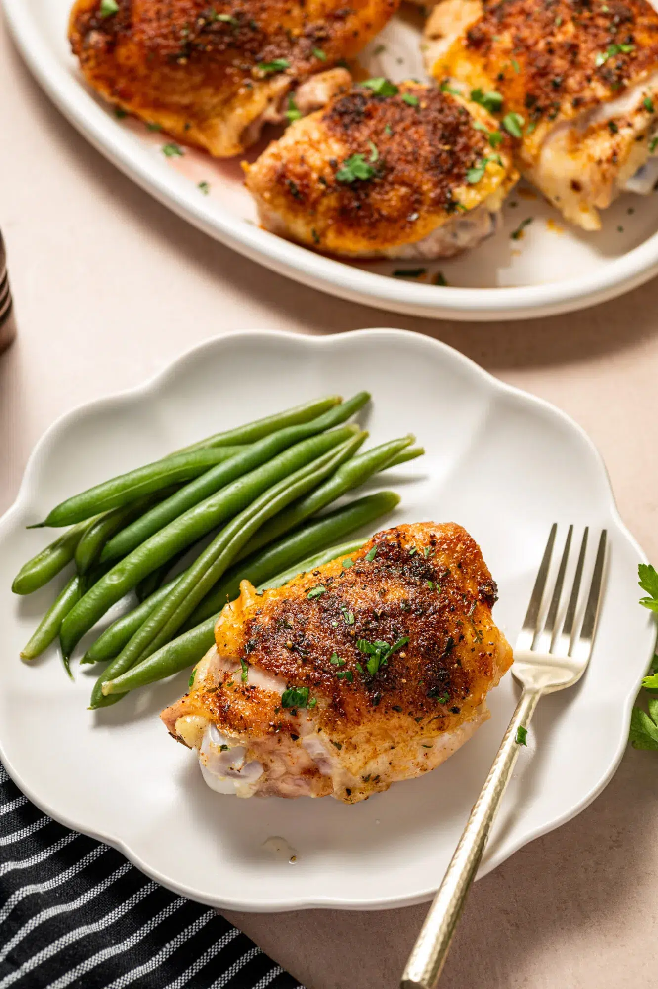 An oven roasted chicken thigh on a white plate with a side of green beans.