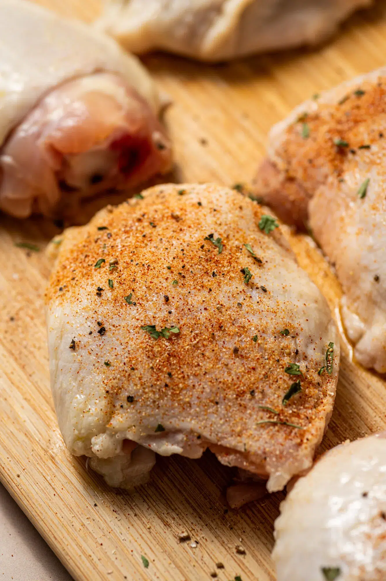 Close-up of a raw chicken thighs seasoned and garnished with parsley.