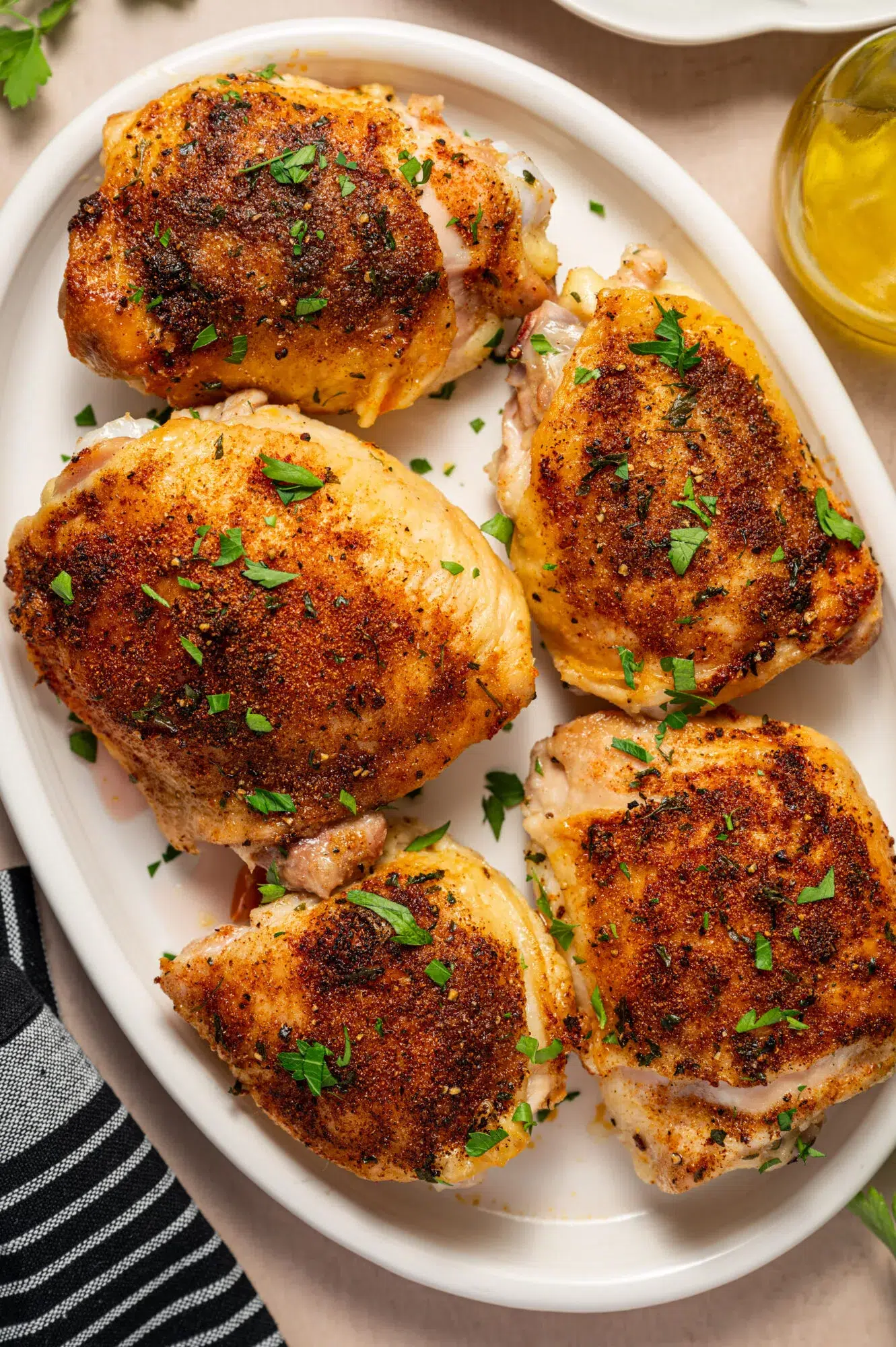 Oven roasted chicken thighs on a white serving plate garnished with parsley.