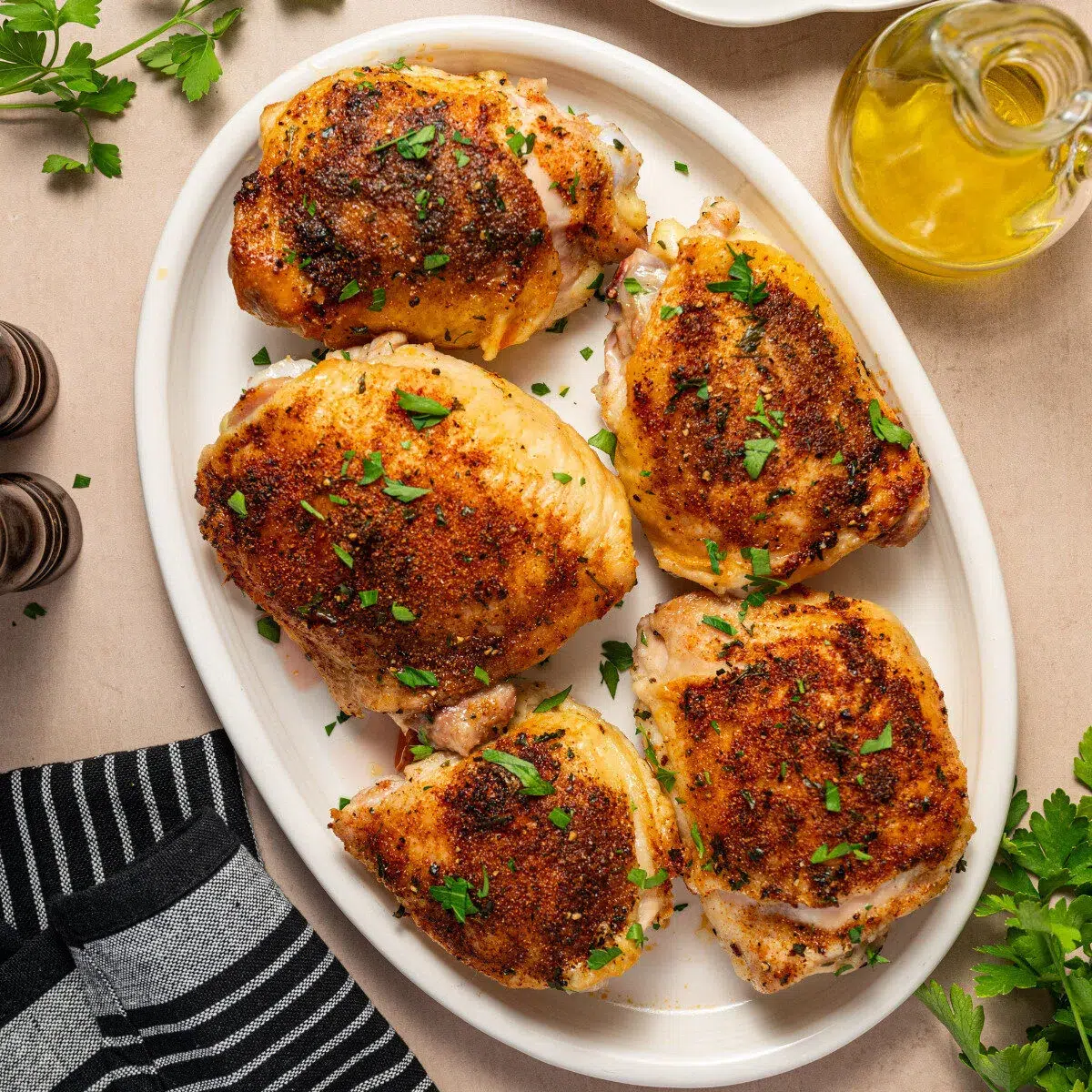 Oven roasted chicken thighs on a white serving plate garnished with parsley.
