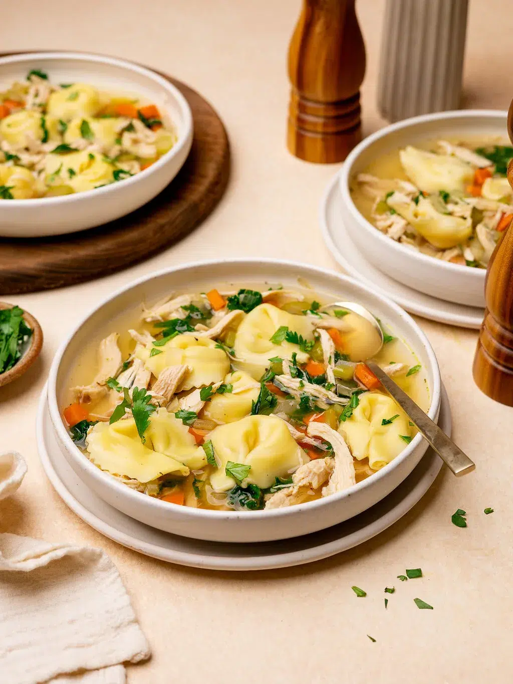 A bowl of chicken tortellini soup with two more bowls in the background.