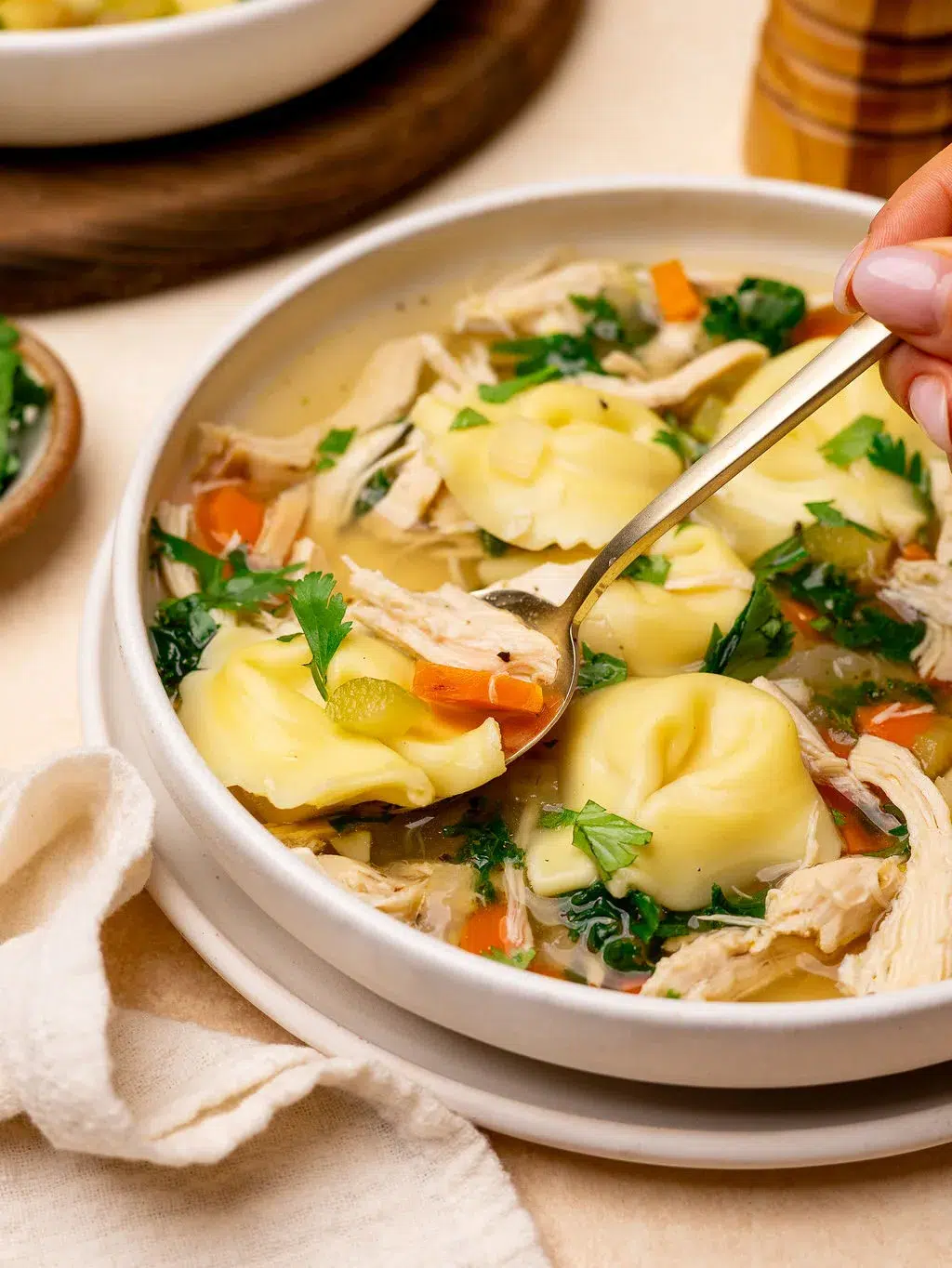 Dipping a spoon into a bowl of chicken tortellini soup.
