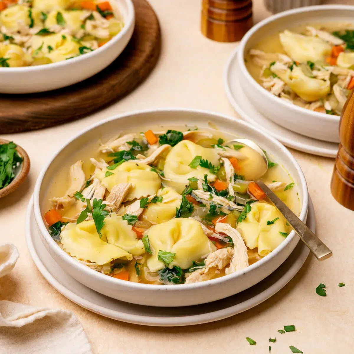 A bowl of chicken tortellini soup with two more bowls in the background.