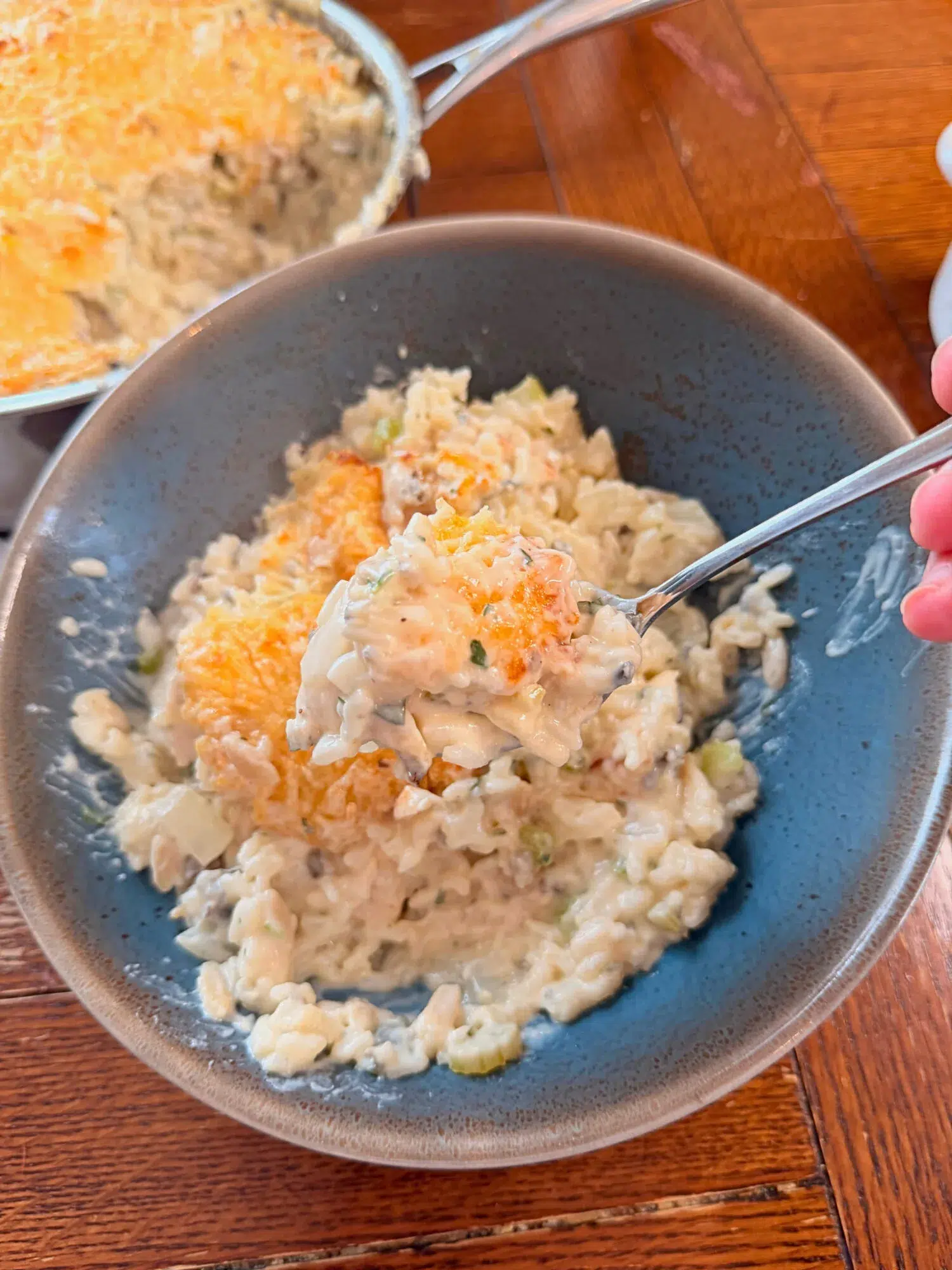 A forkful of chicken wild rice bake hovering over a blue bowl.