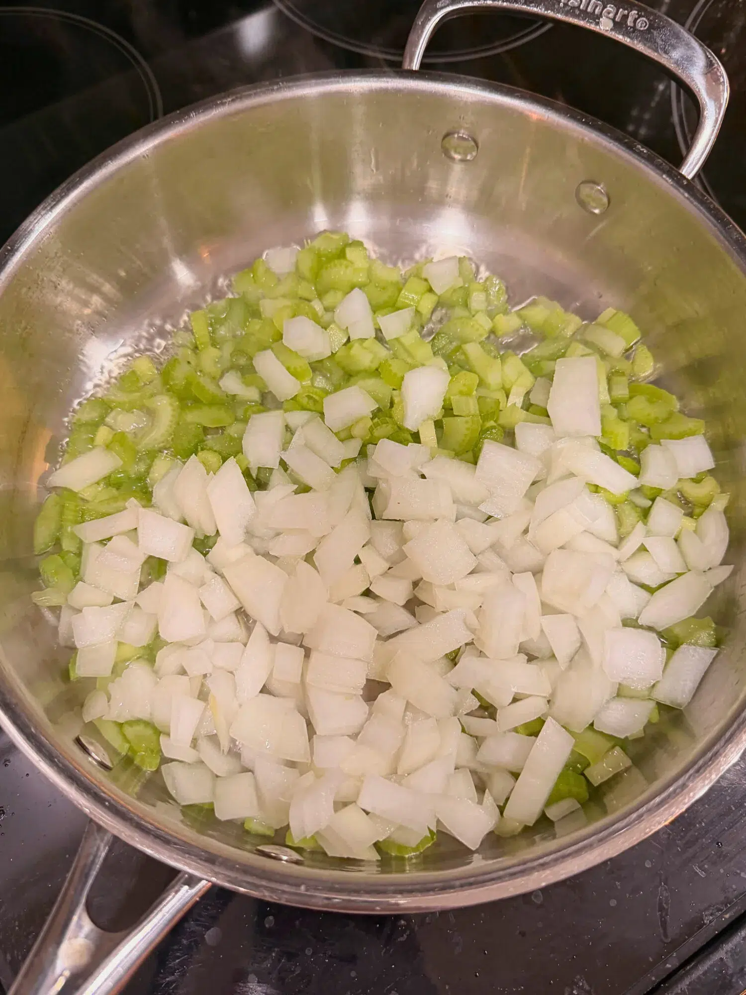 Onions, celery, and garlic in a pan cooking with oil.