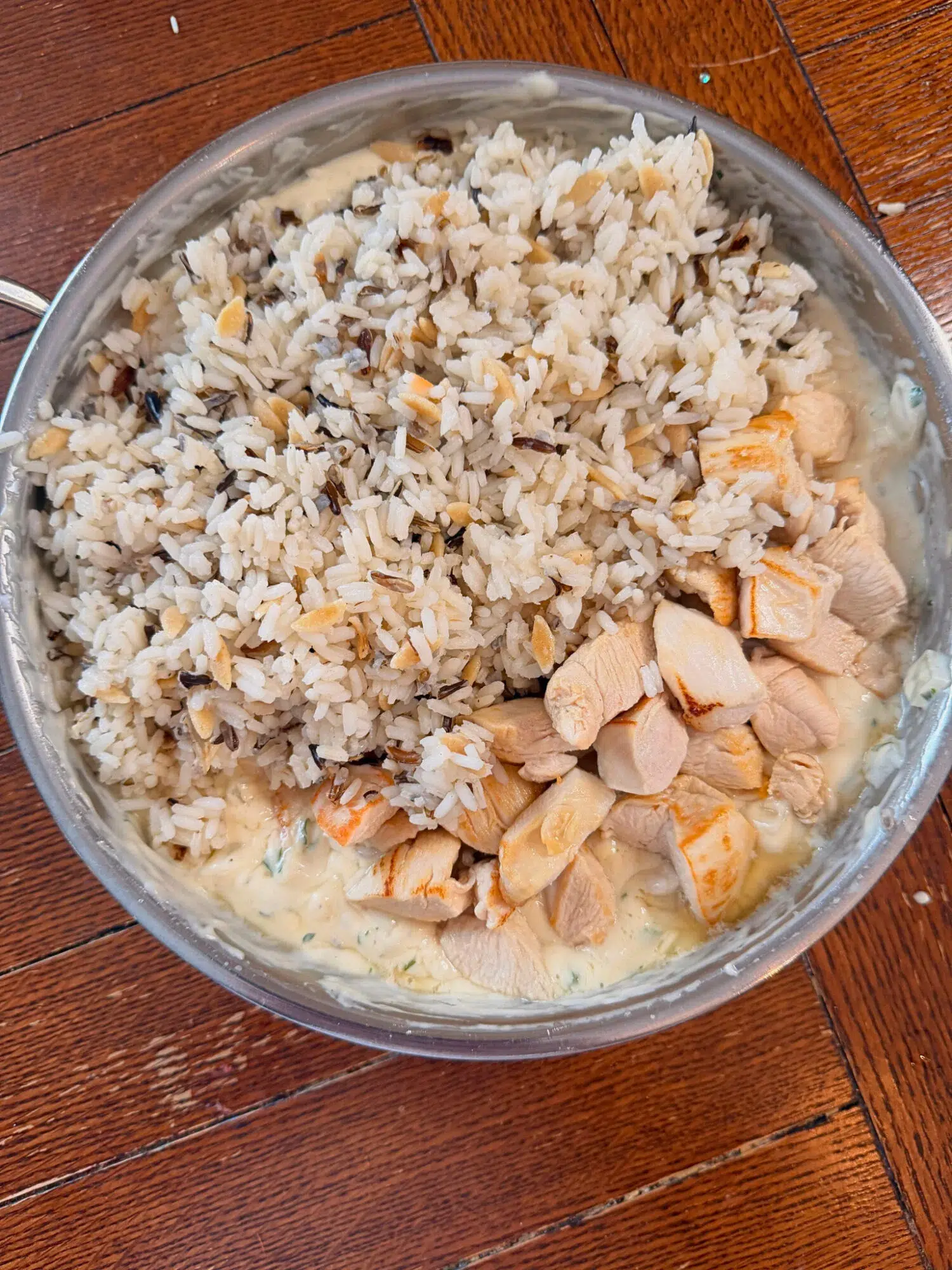 Adding cooked chicken and wild rice to a pan of creamy veggie sauce.