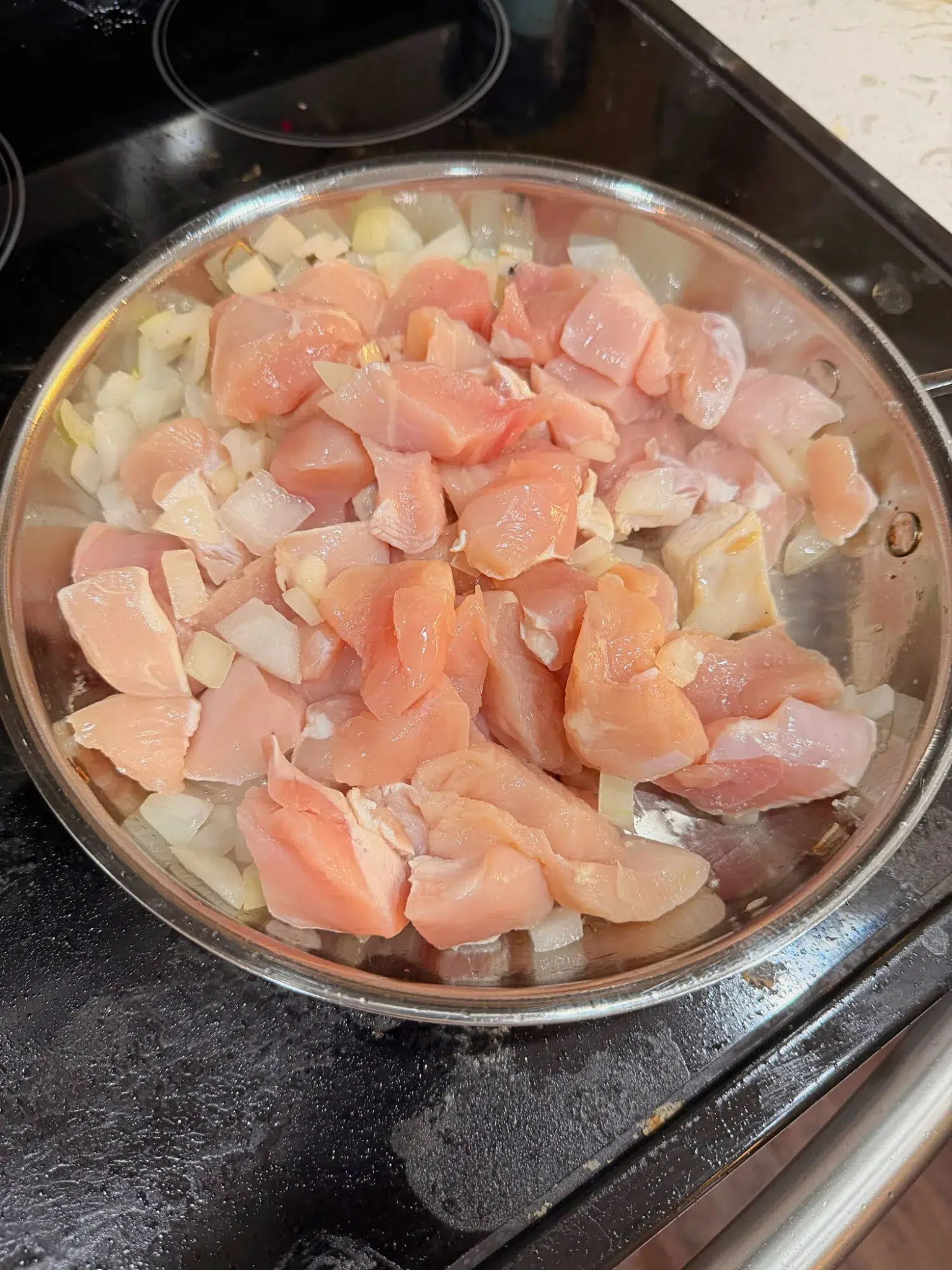Chicken pieces searing with onions in a pan.