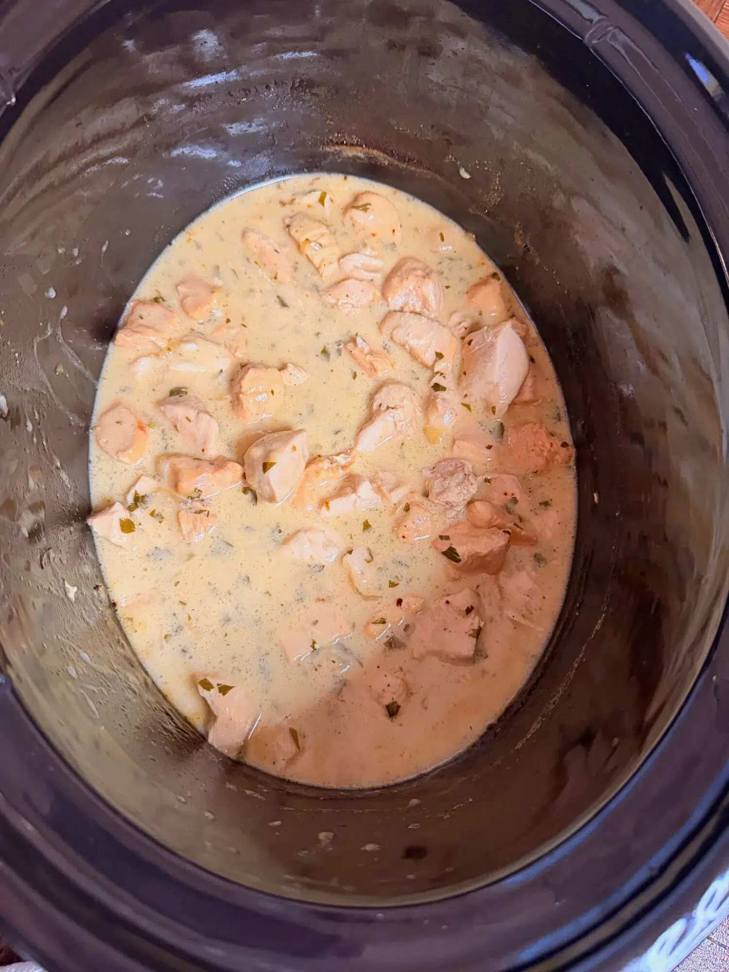 Chicken pieces cooking with sauce in a slow cooker.