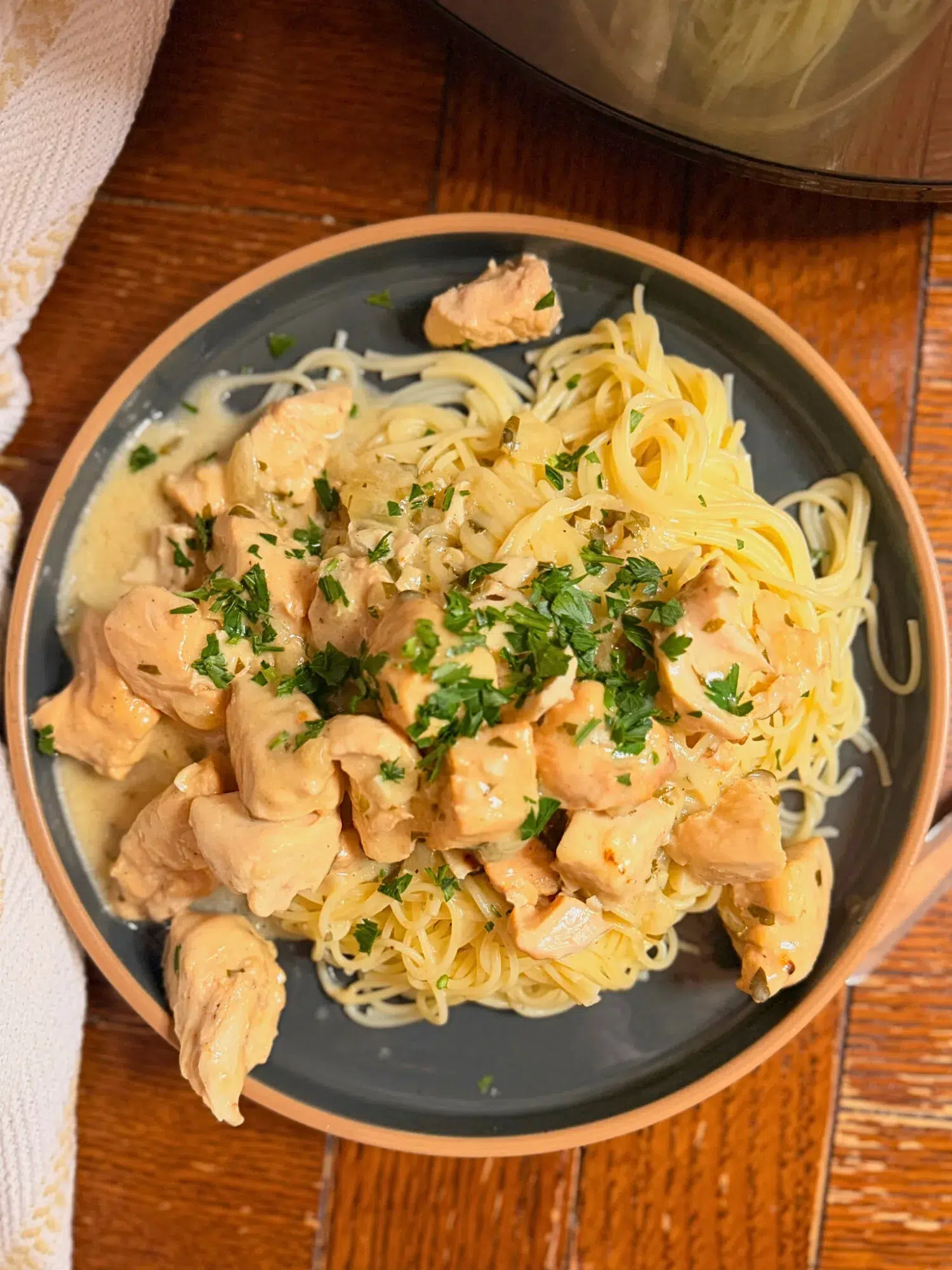 Slow cooker creamy garlic chicken served over a plate of noodles.
