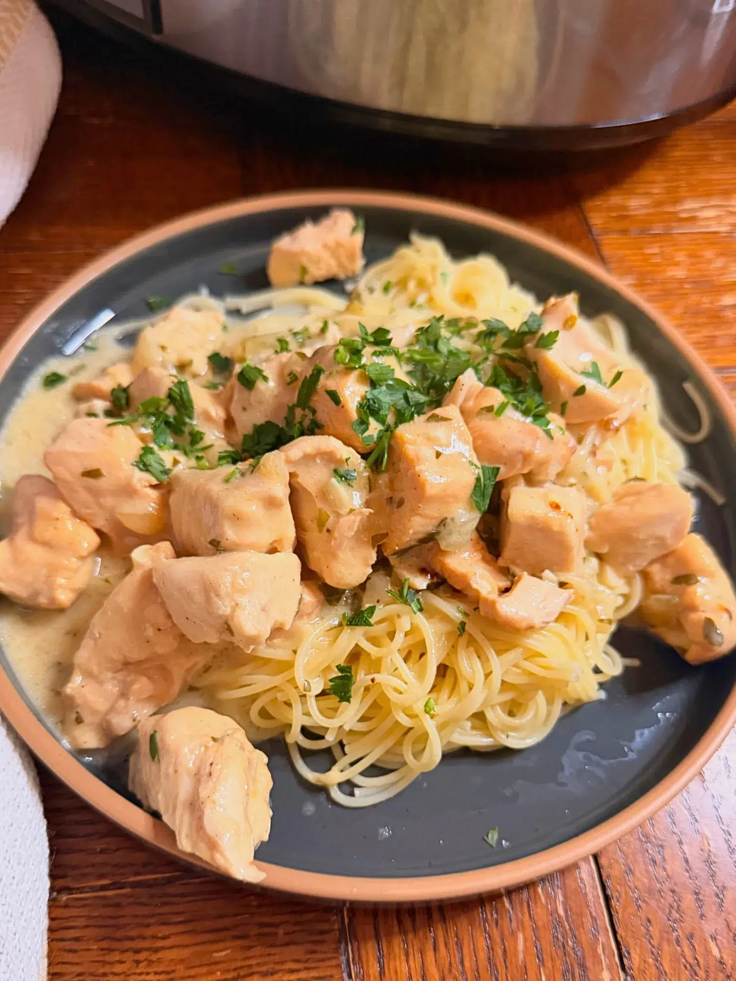 Slow cooker creamy garlic chicken served over a plate of noodles.