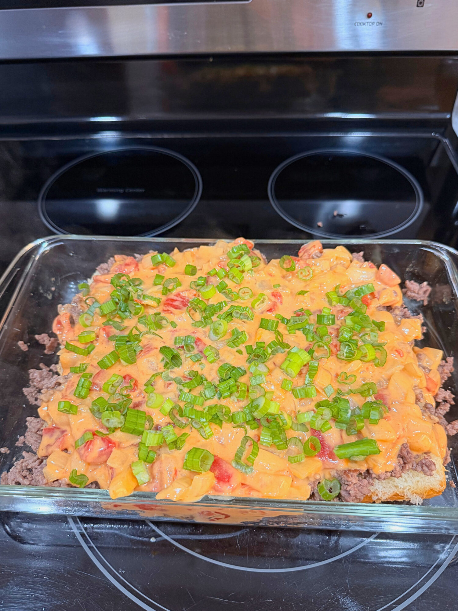 Layering on green onions to ground beef queso sliders.