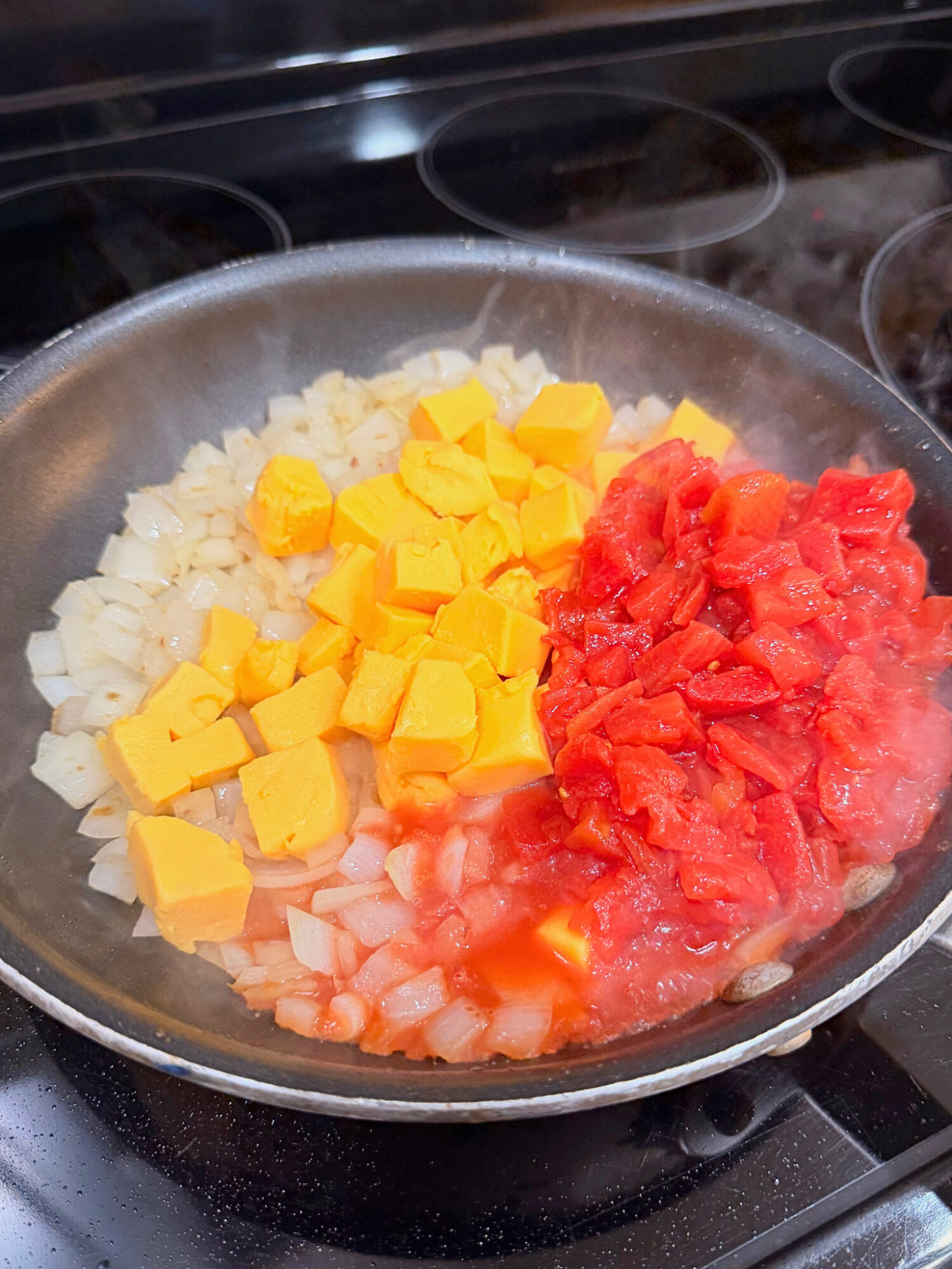 Blocks of Velveeta cheese, diced tomato, and onion in a skillet.