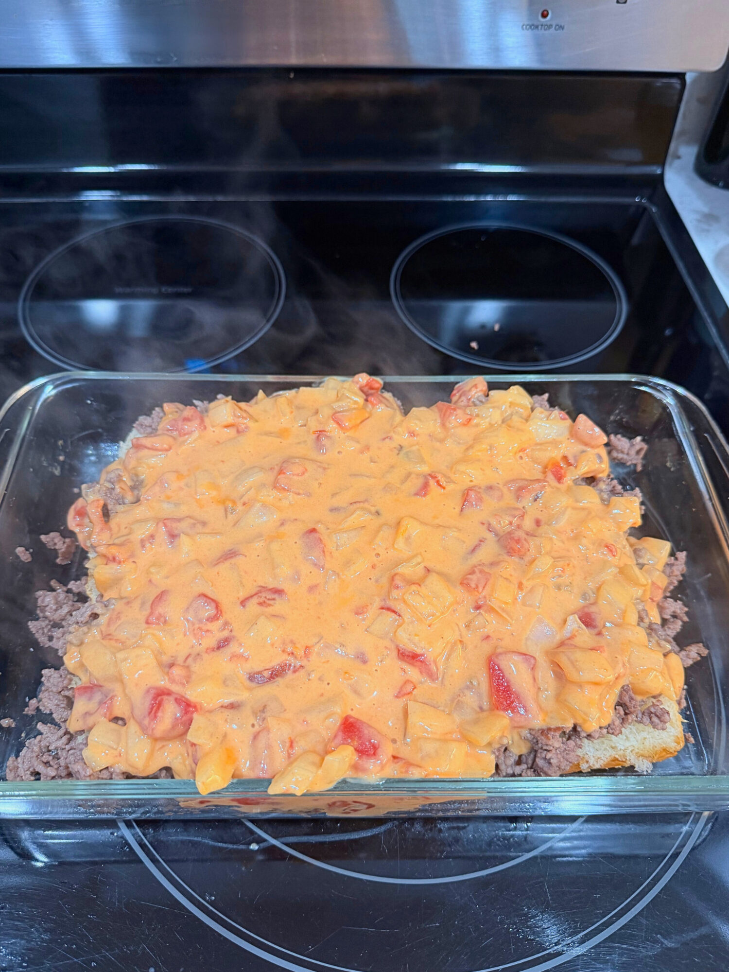 Layering Velveeta cheese sauce onto ground beef queso sliders.